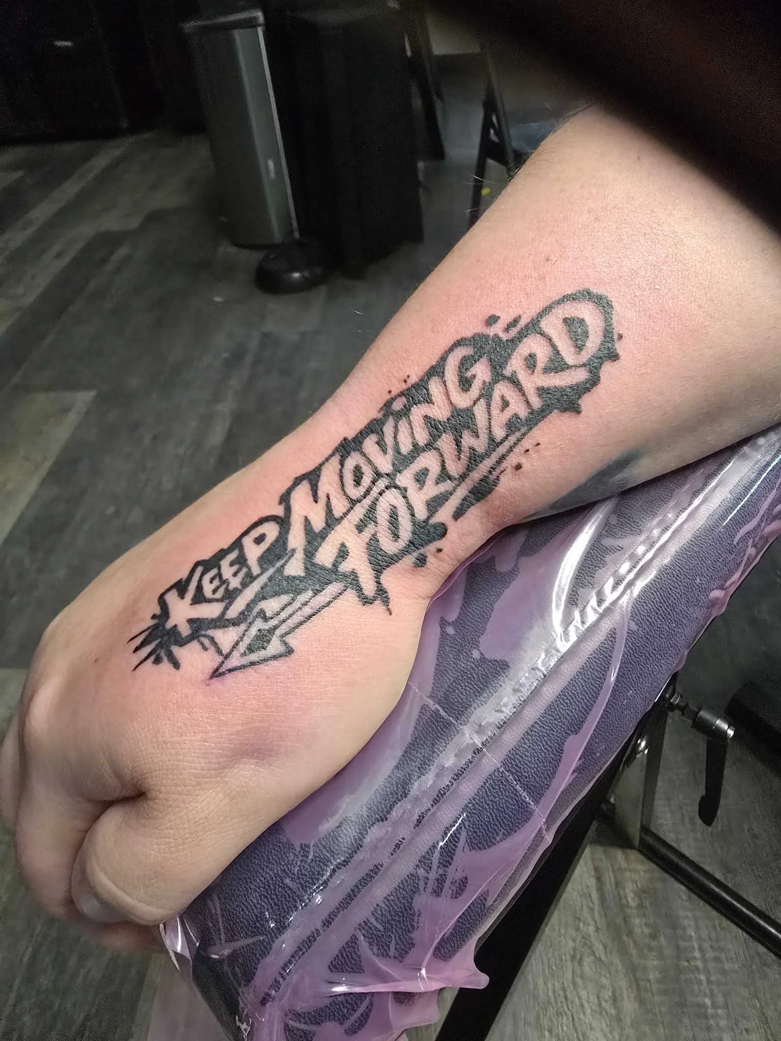Tattoo on forearm with the words "Keep Moving Hard" in stylized font and decorative elements
