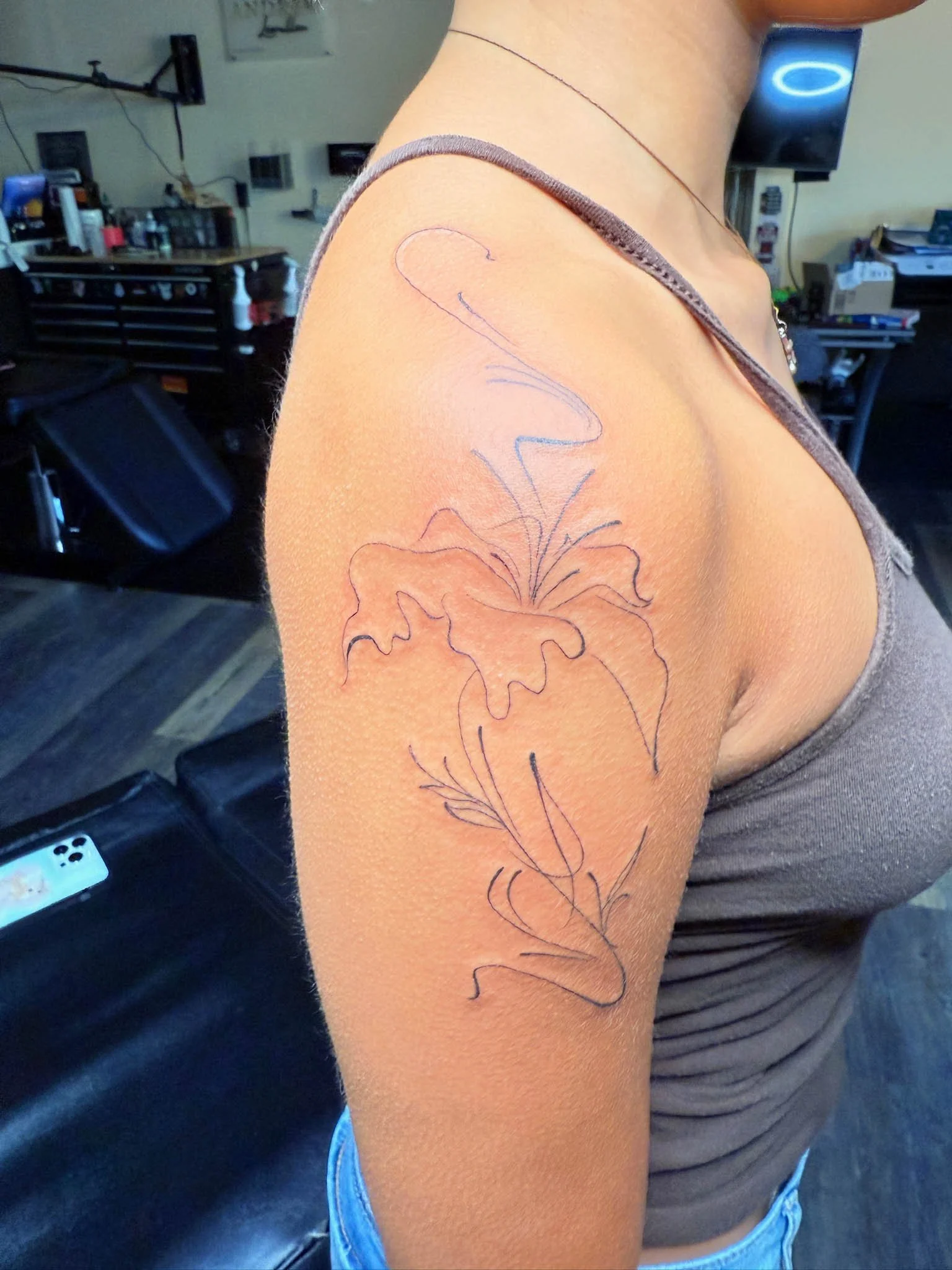 A person with a tattoo stencil of a floral design on their upper arm in a tattoo parlor.