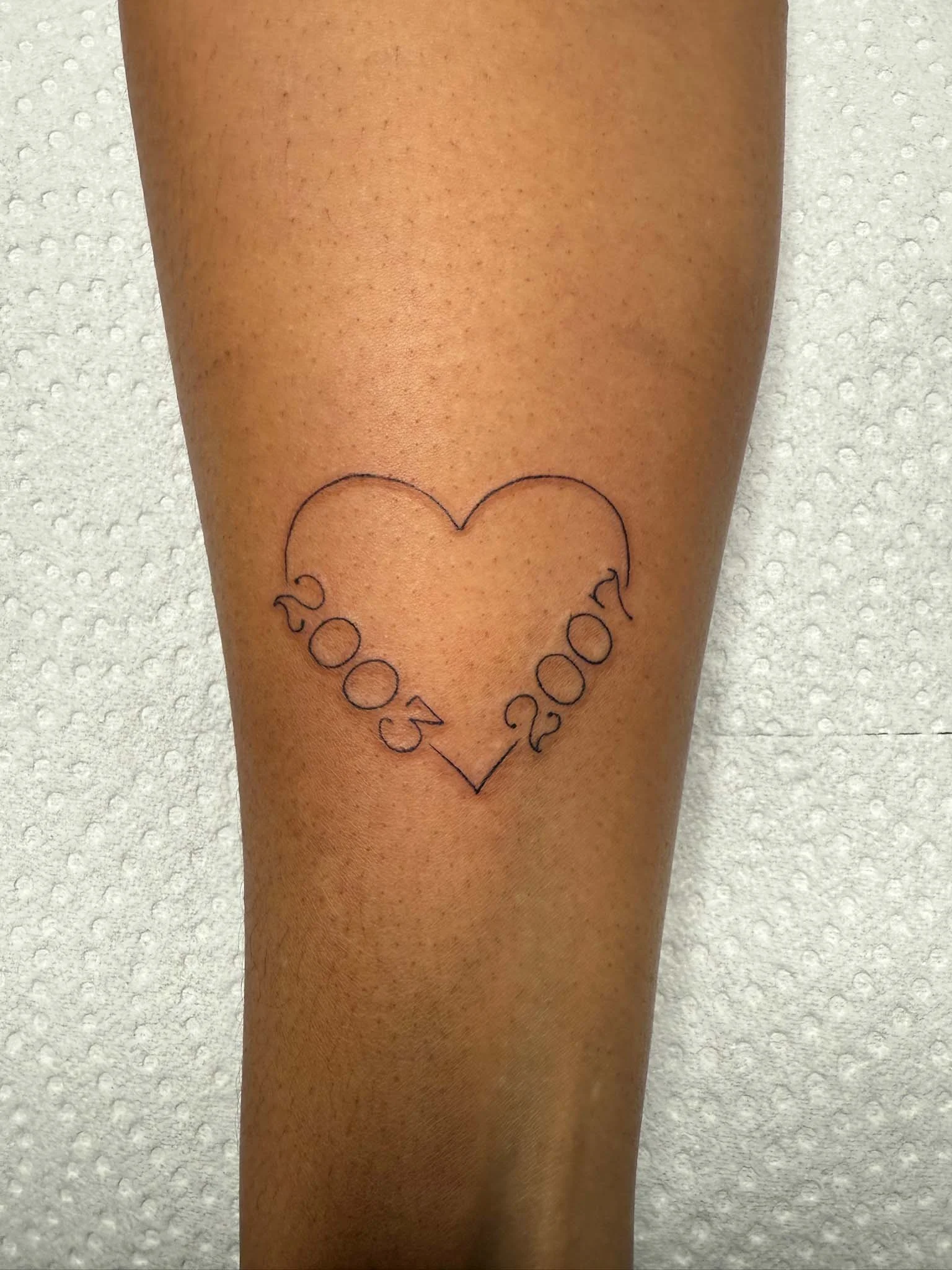 Tattoo of an outline of a heart with the year 2005 on the left side and 2007 on the right side.
