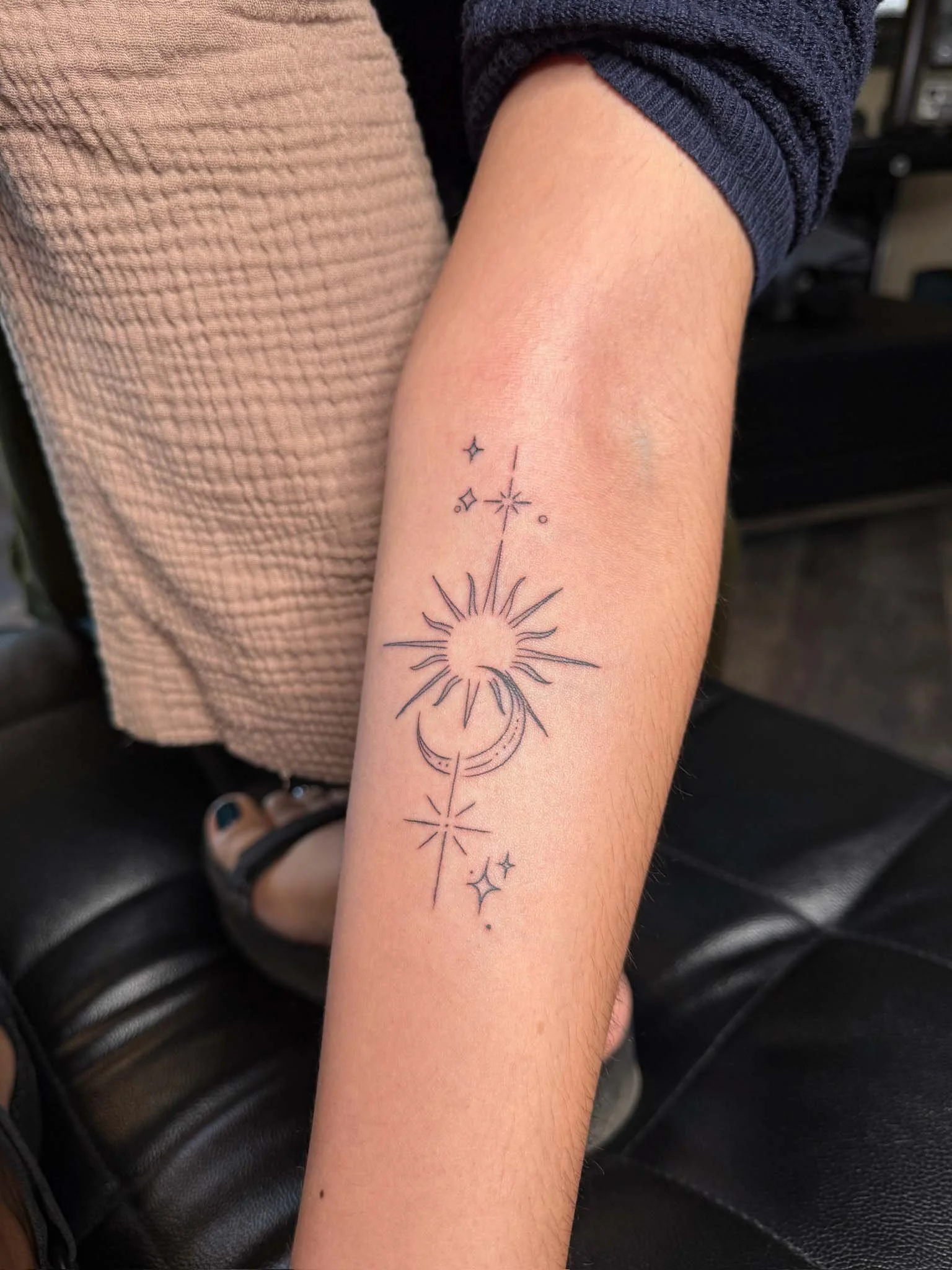 Tattoo of a sun with rays, a crescent moon, and stars on a person's forearm.