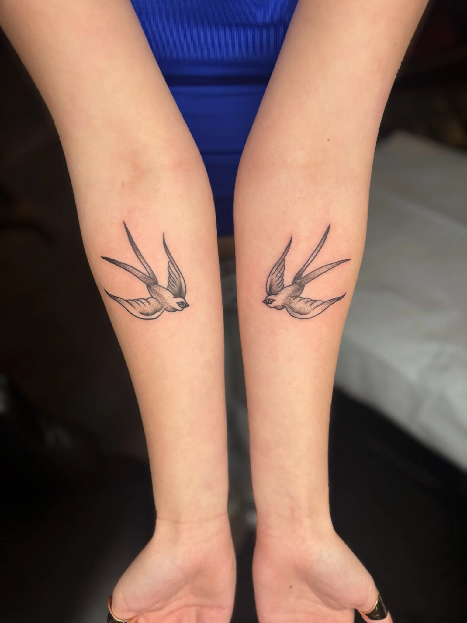 Two person's forearms with matching swallow bird tattoos facing each other.