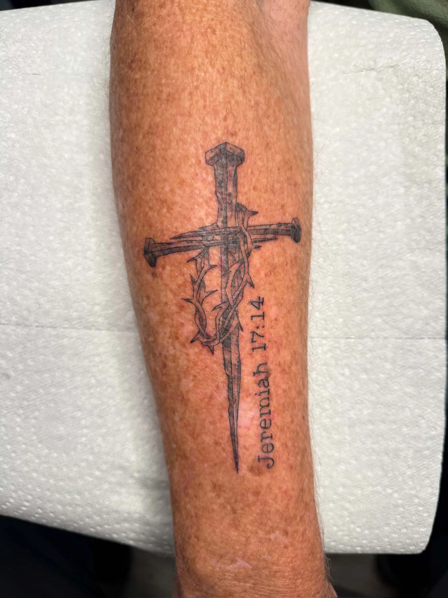 A tattoo of a cross with a sword and thorny vines, and the words 'Jeremiah 17:14' written vertically.