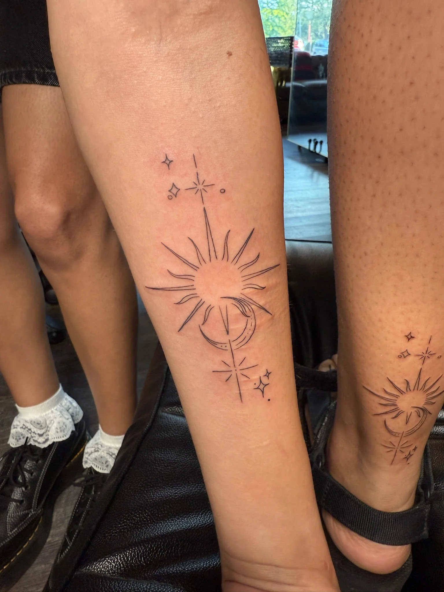 Tattoo of a celestial design featuring a sun, moon, stars, and geometric lines on a person's leg.