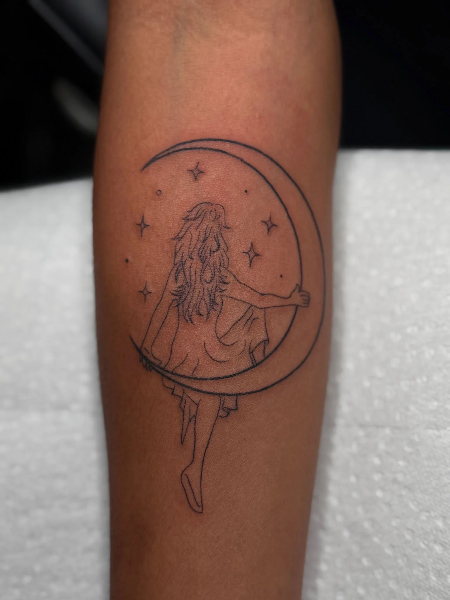 Tattoo of a girl sitting on a crescent moon surrounded by stars.