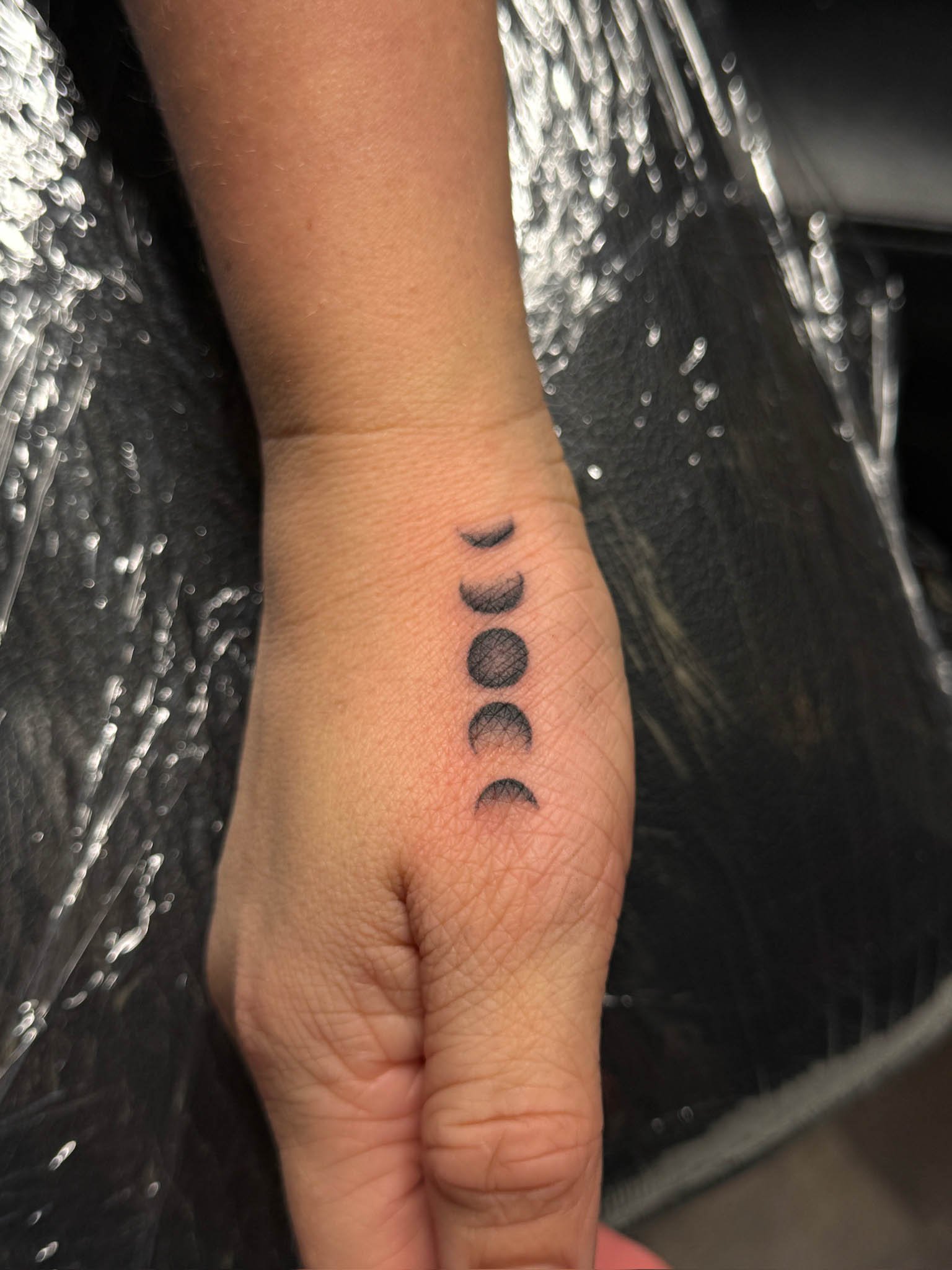 Tattoo of the moon phases on a person's inner wrist.