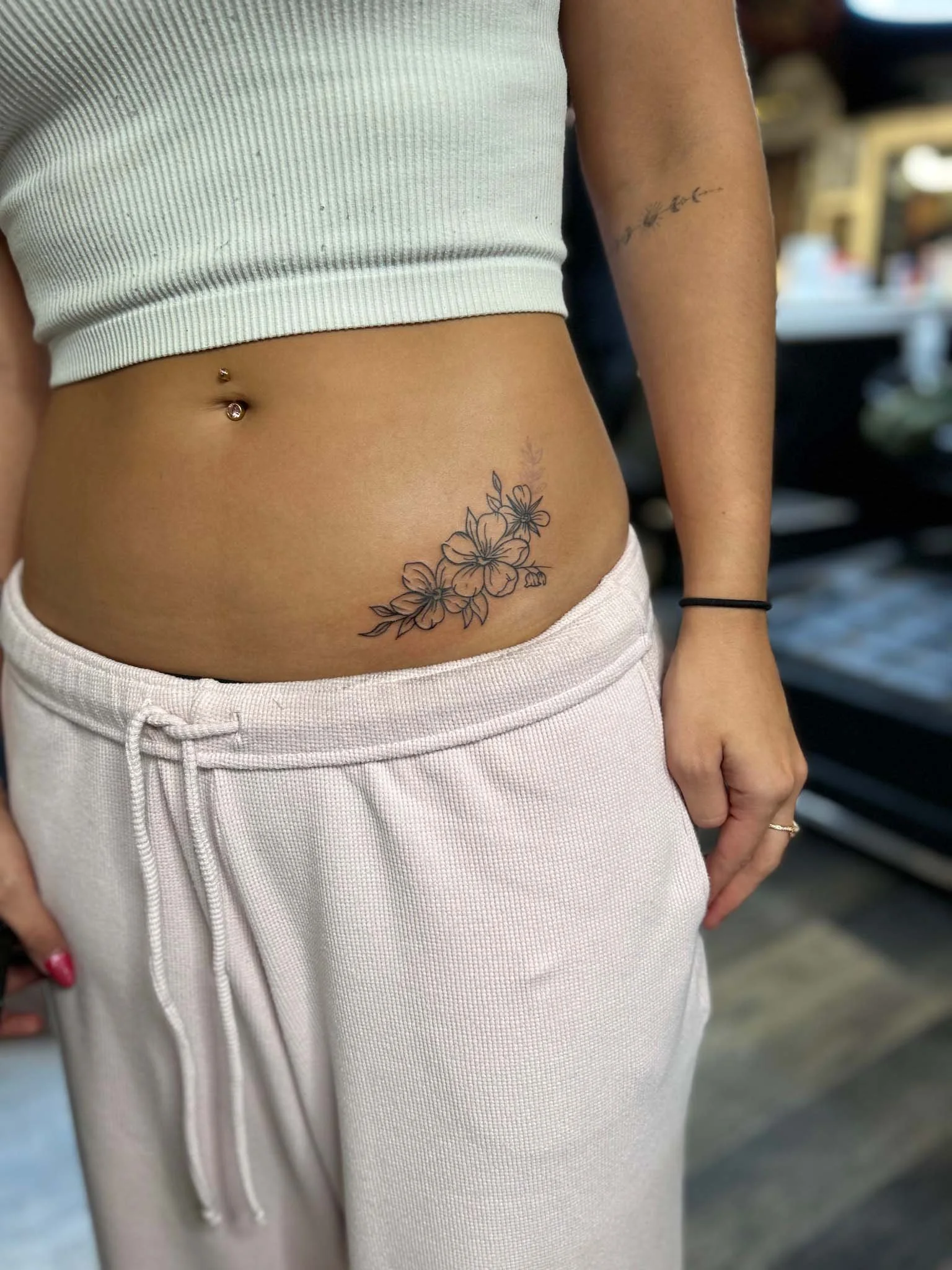 Delicate floral vine tattoo running along a woman's hip and lower abdomen