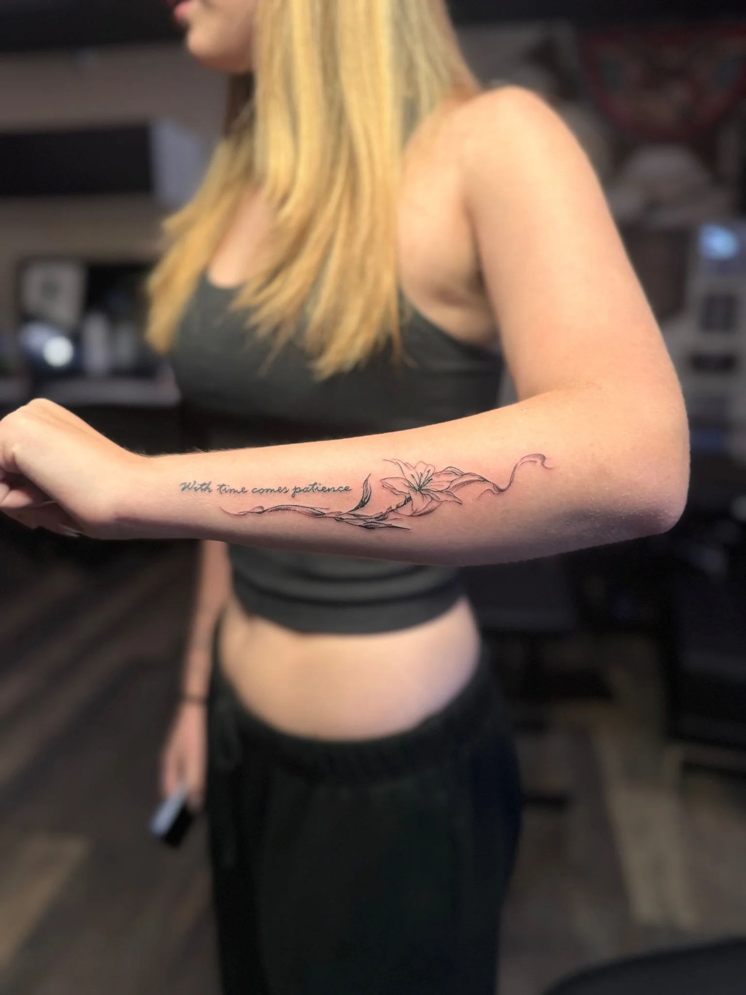 Woman in a dark top displaying a side forearm tattoo.