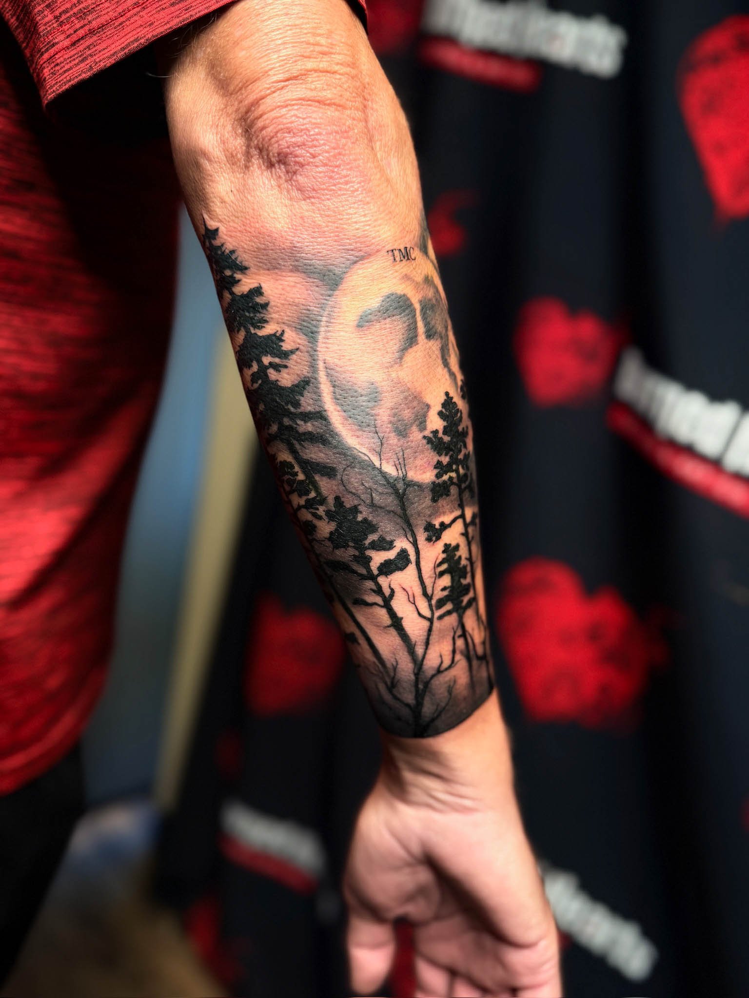 Tattoo sleeve featuring trees, a moon with a skull face, and the words 'TMC'.