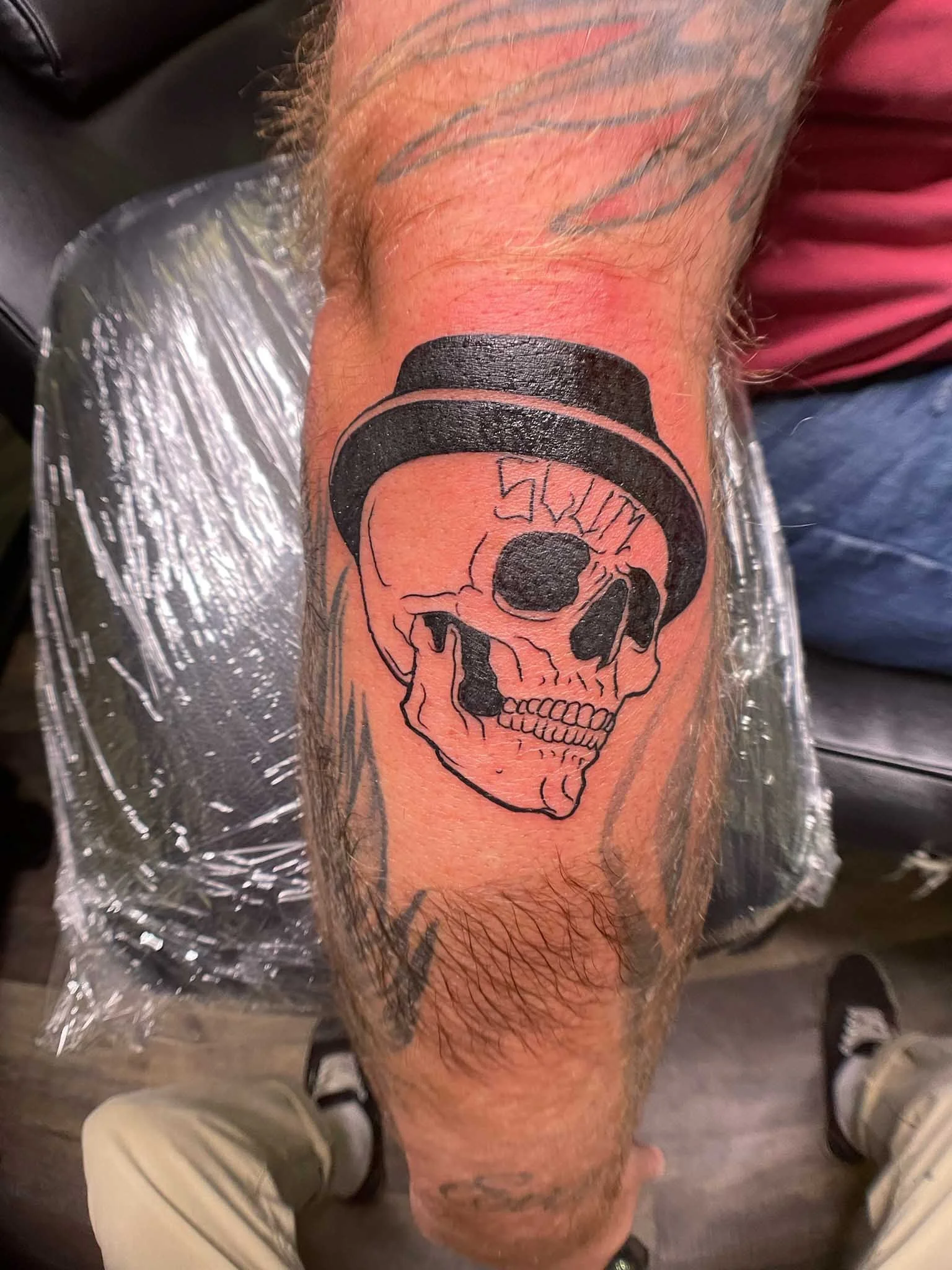 Black outline tattoo of a skull wearing a top hat on a person's forearm.