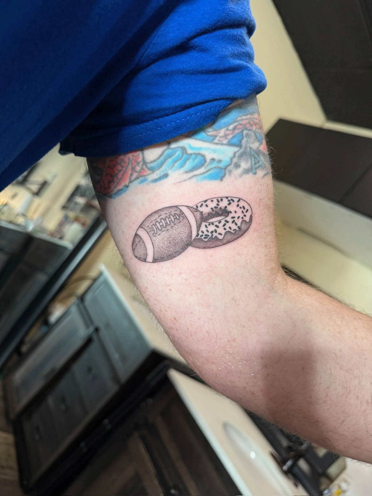 Tattoo of a football and a donut on a person's upper arm.