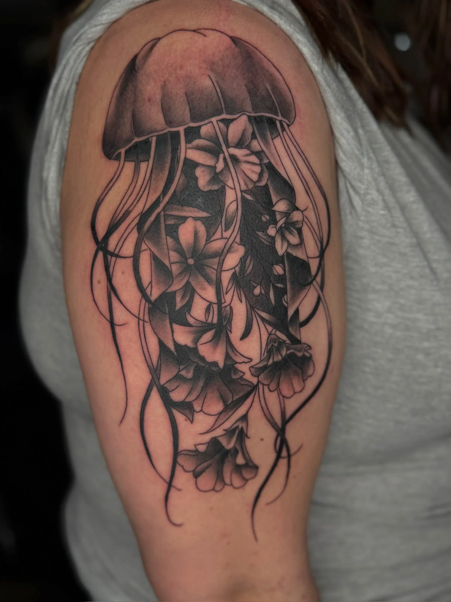 Tattoo of a jellyfish with flowers and flowing tentacles on a person's upper arm.