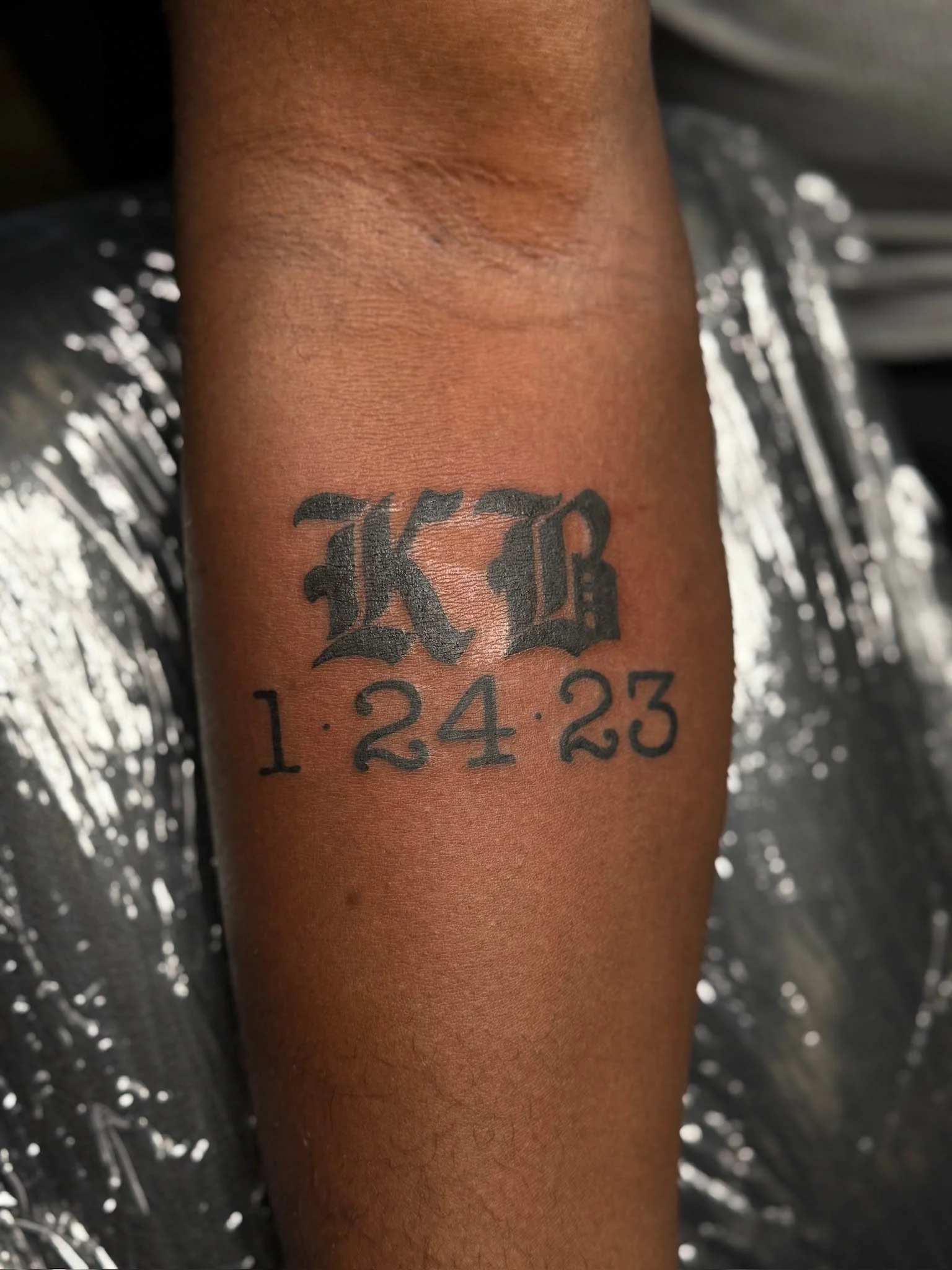 Tattoo on forearm with initials 'K L B' above the date '1.24.23'.