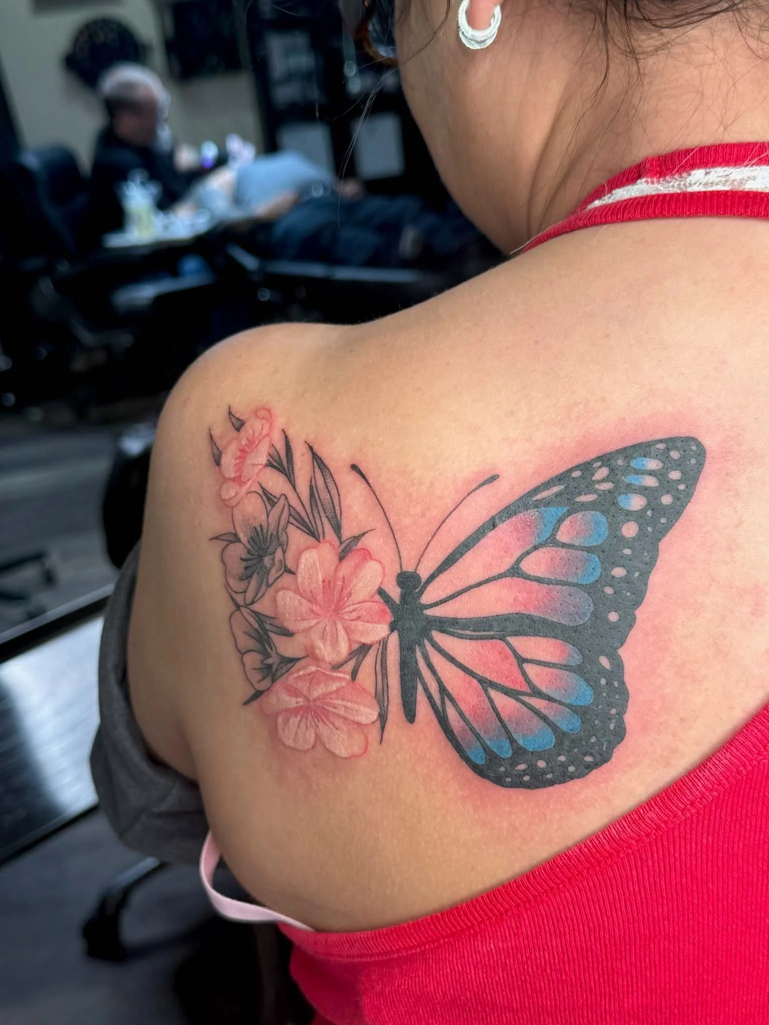 Tattoo of a butterfly with black and blue wings and pink flowers on the person's shoulder.