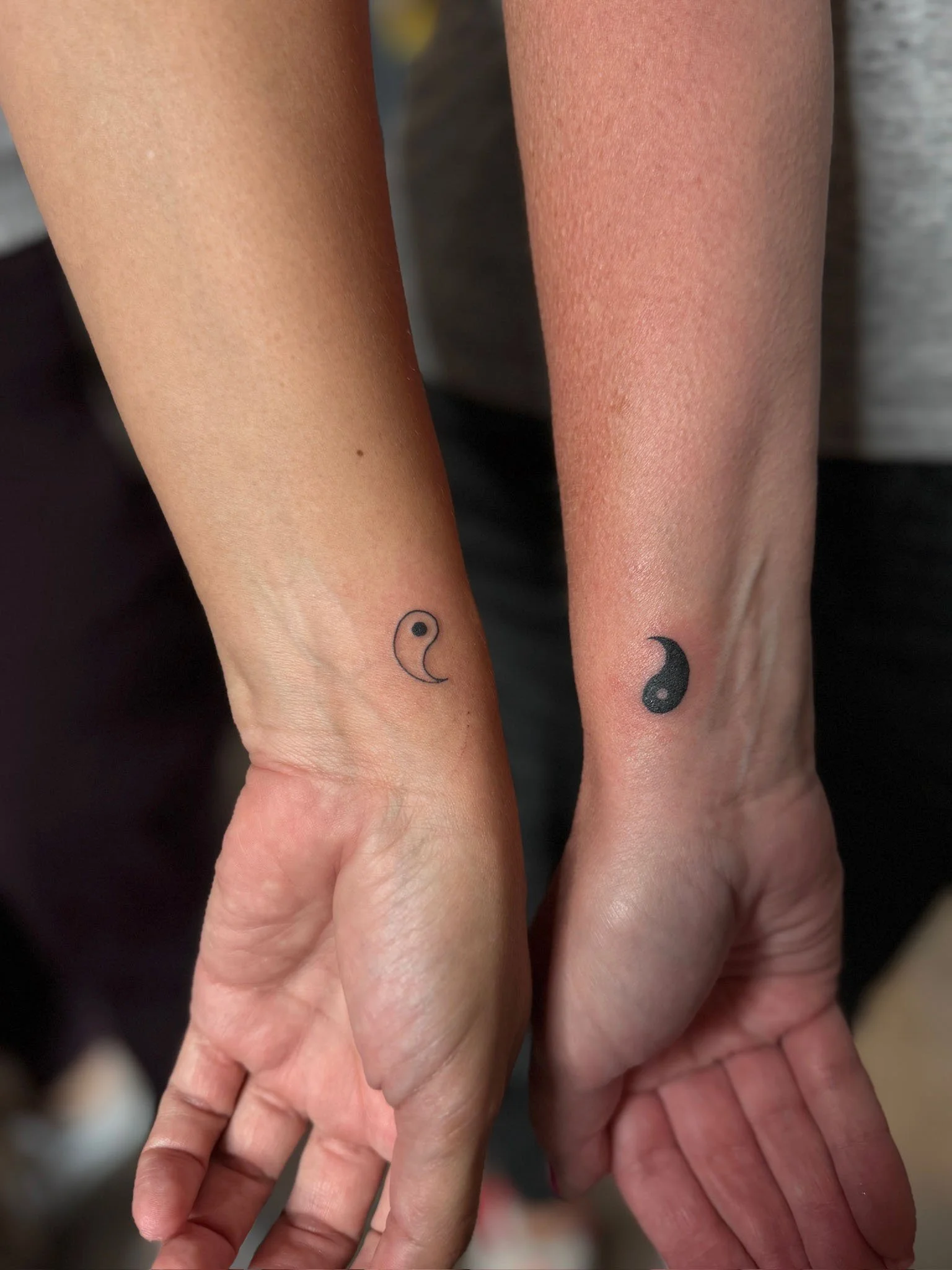 Close-up of two hands with matching yin-yang moon tattoos on their wrists, symbolizing harmony and balance.