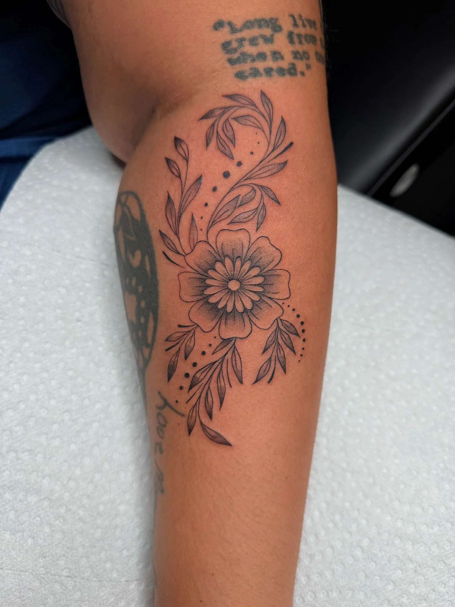 A floral tattoo on a person's forearm featuring a large flower with leaves and small decorative dots.