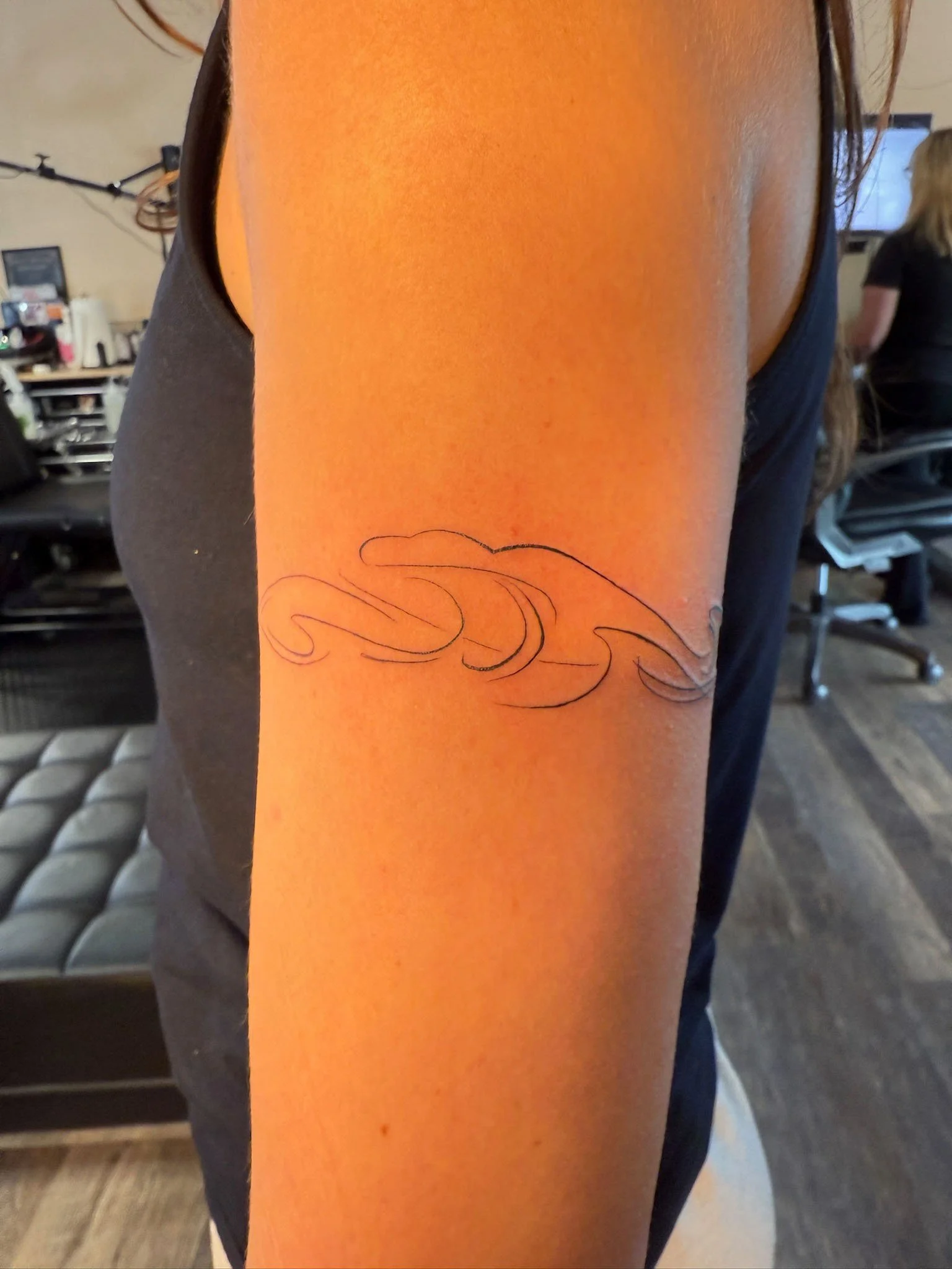 A person's inner upper arm with a new tattoo of stylized clouds in black ink.