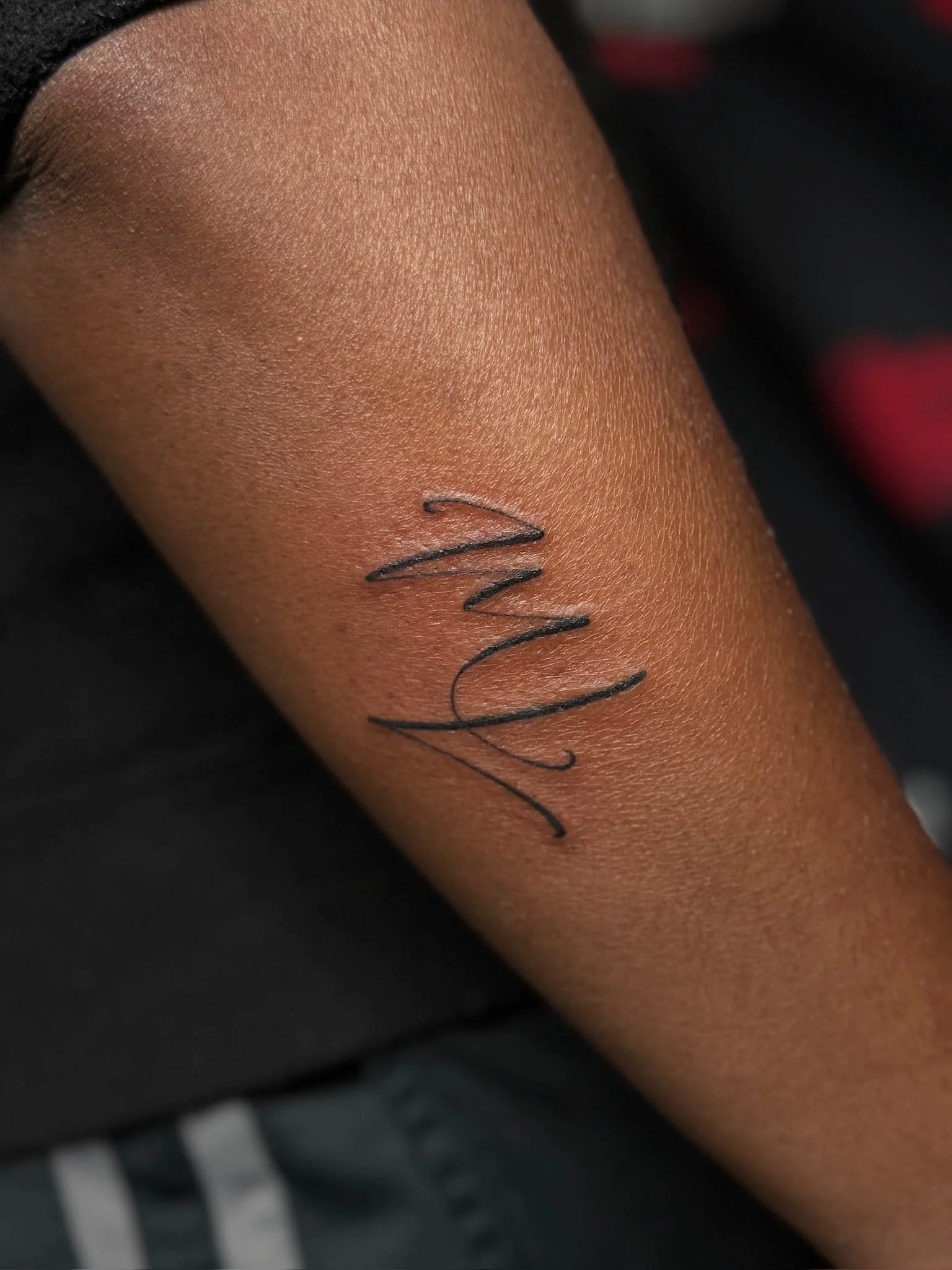 Close-up of a person's arm with a black cursive tattoo reading 'Mum' on its inner side.