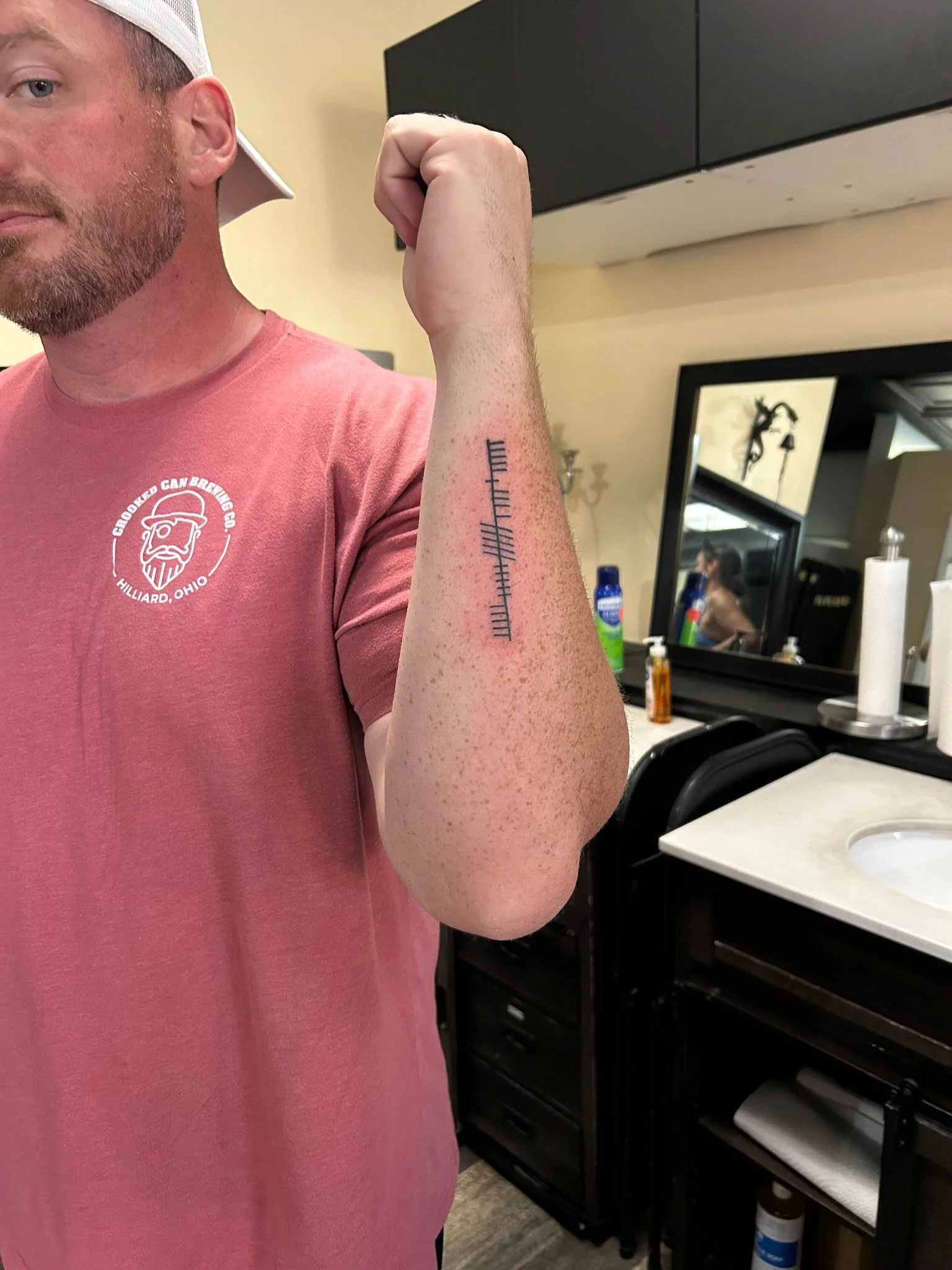 Man in a pink t-shirt displaying handwritten script lettering on his forearm.