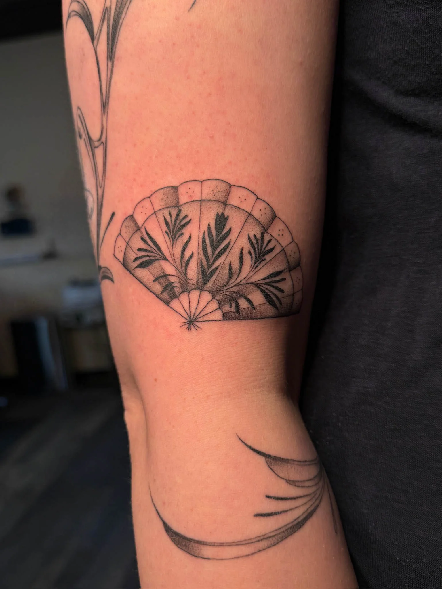 Tattoo of a decorative fan with floral and leaf design on a person's arm.