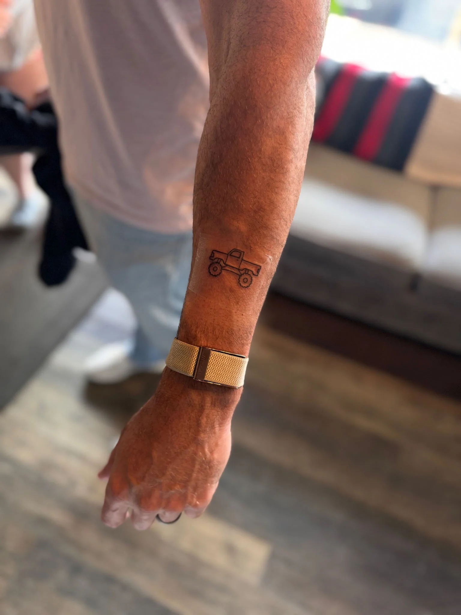 Minimalist fine-line tattoo of a lifted pickup truck on a person's inner forearm