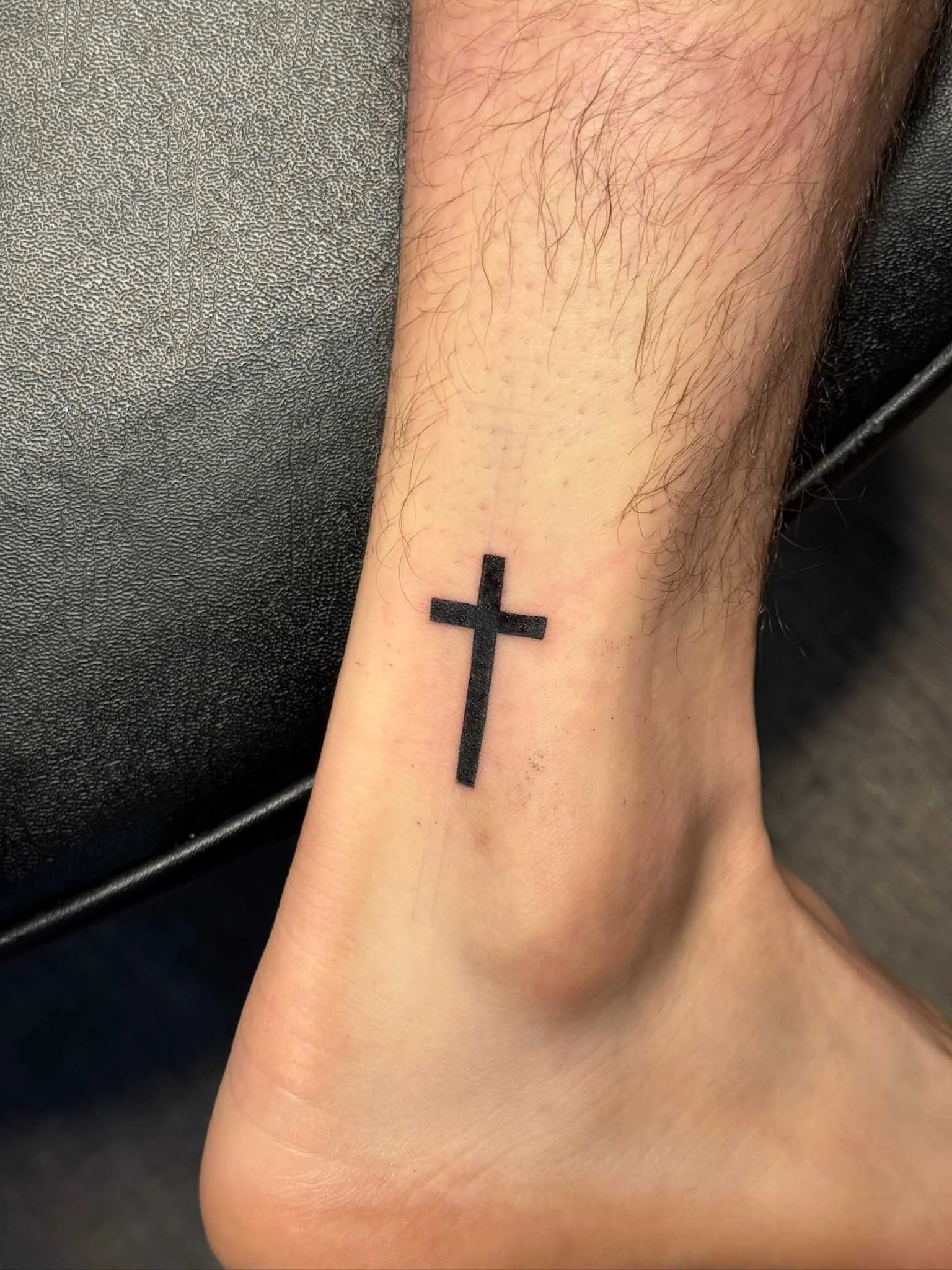 Tattoo of a black cross on the ankle.