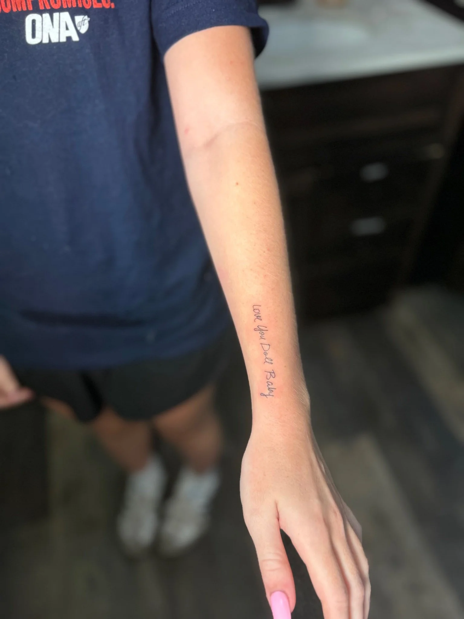 Person in a navy shirt displaying a fine-line forearm tattoo