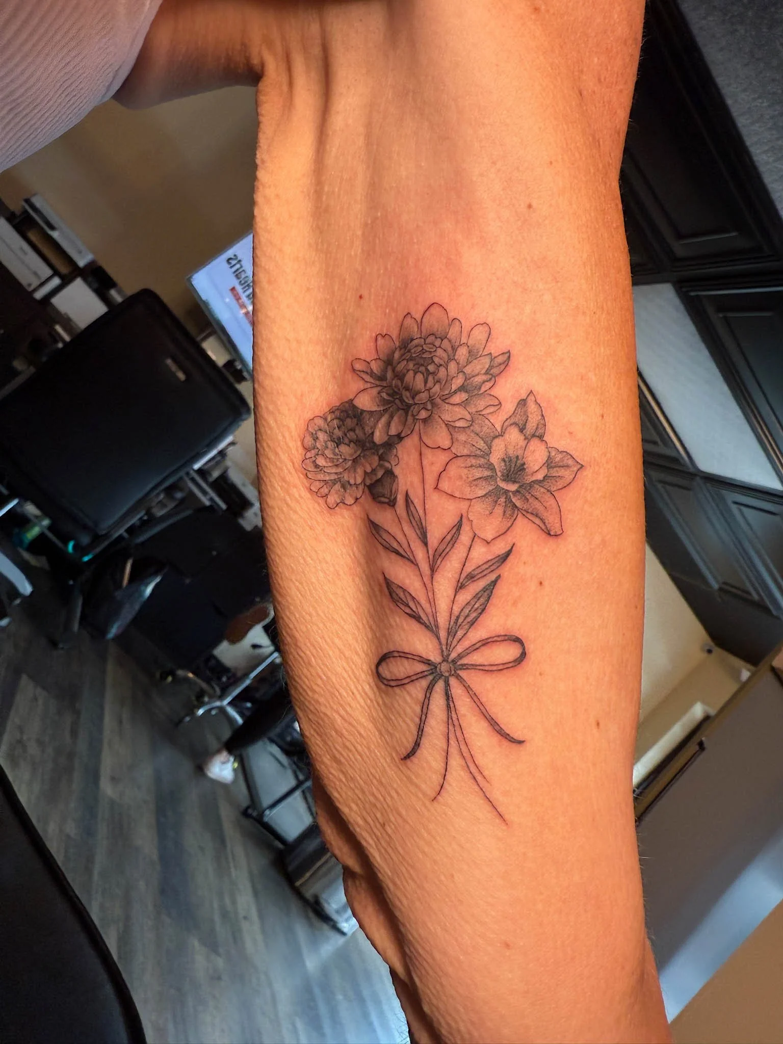A tattoo of a bouquet of flowers including a large daisy and a smaller flower, tied with a string bow on a person's inner forearm.