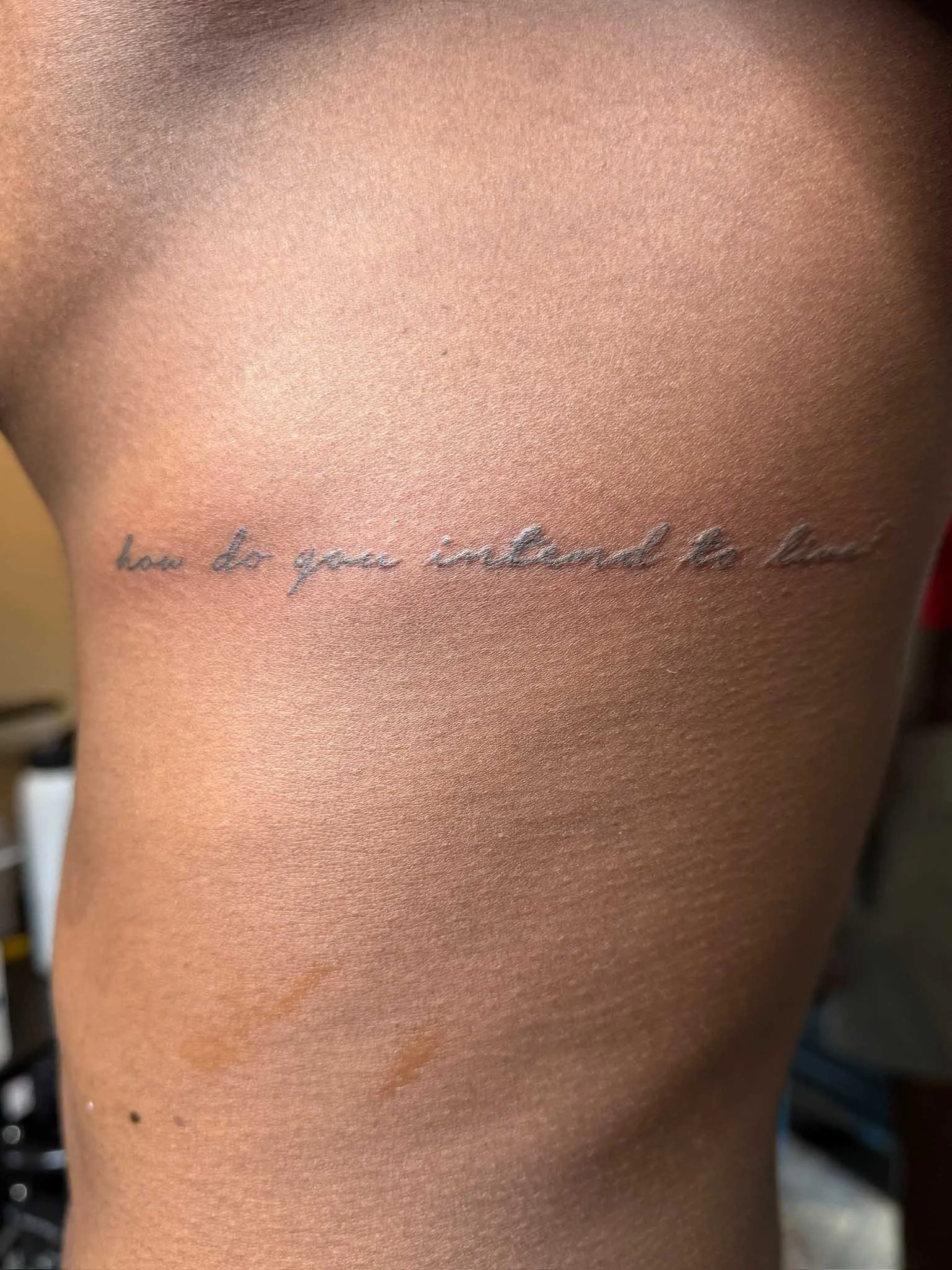 Close-up of a person's side torso with a tattoo that reads 'how do you understand so much' in fine cursive script.
