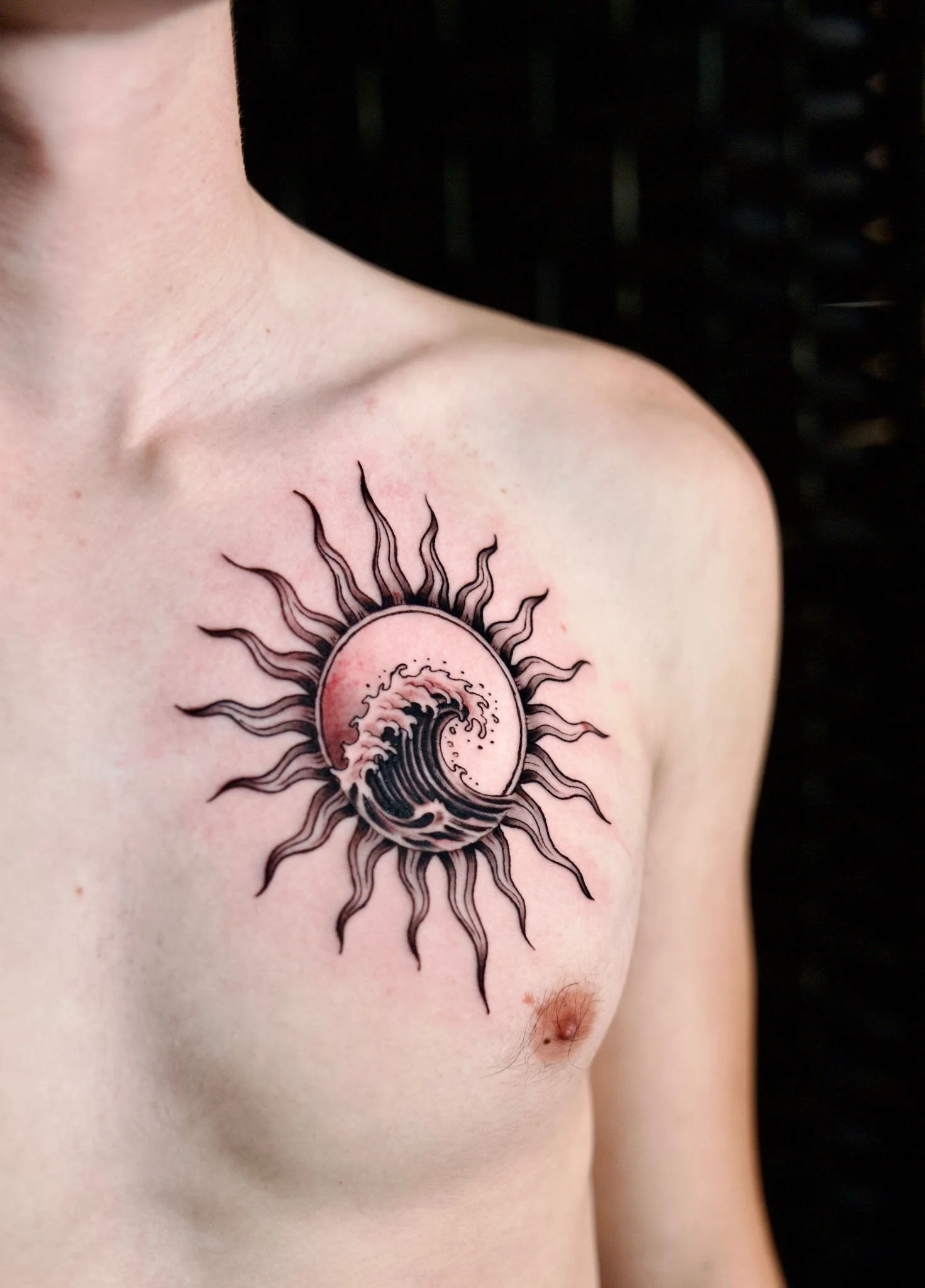 Radiating sun face design with a central eye tattoo on the collarbone