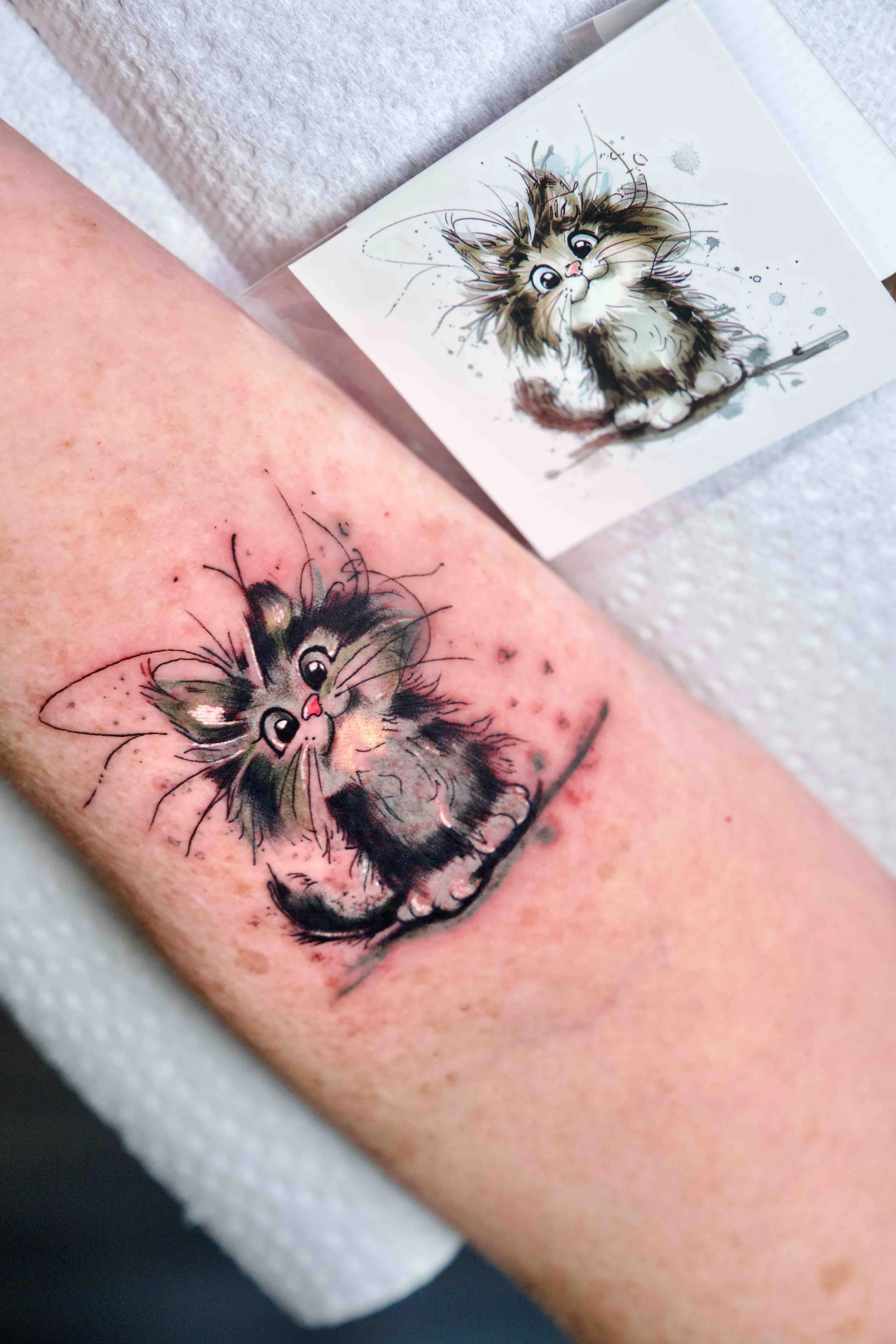 Freshly inked cat portrait tattoo placed next to its original printed paper sketch.
