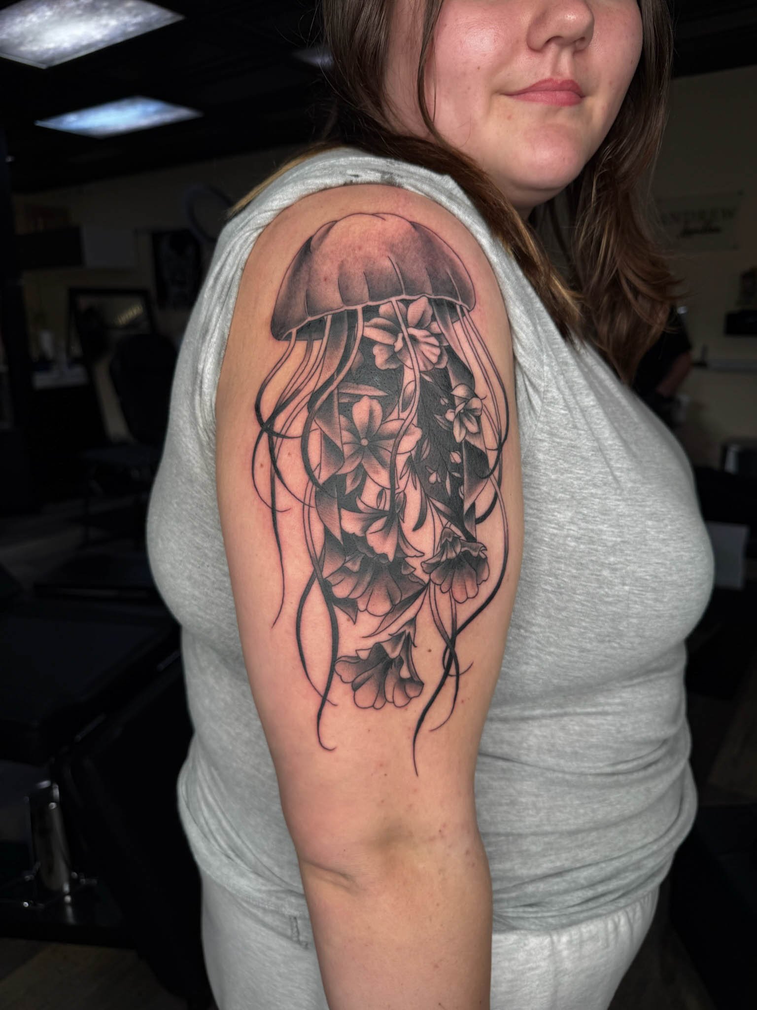 Tattoo of a jellyfish with flowers on a woman's upper arm.