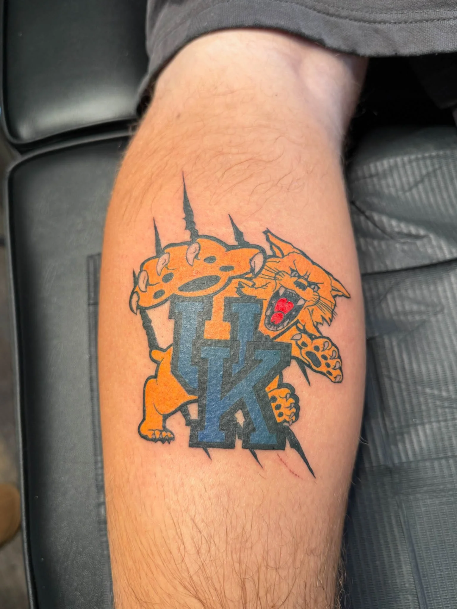 Tattoo of a fierce orange tiger growling, with claws extended, grabbing a hockey stick and the letters 'UK' in bold, black and gray, in the center.