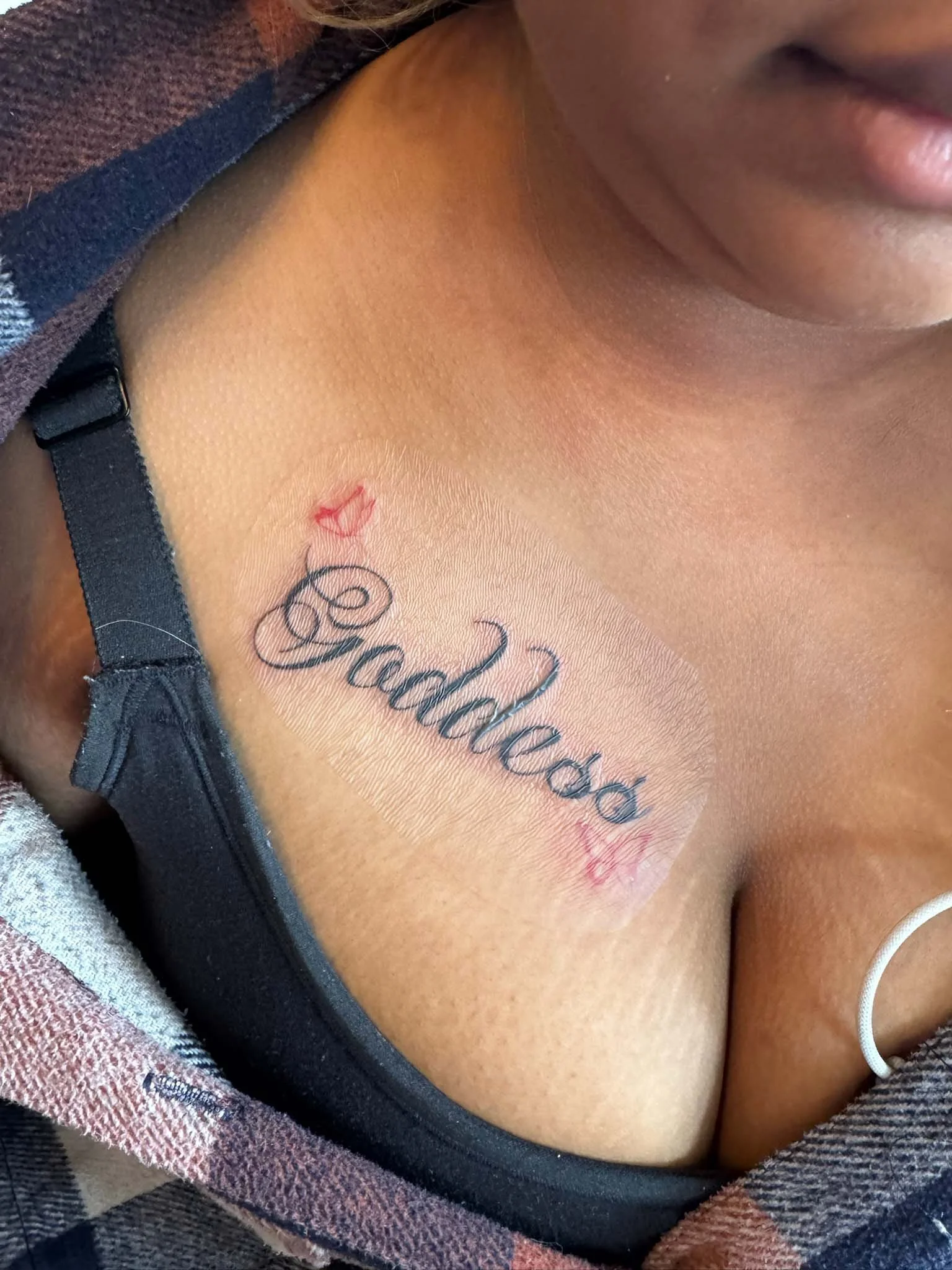 Tattoo on person's chest with the word 'Badass' in cursive and a small red lips design above and below the word.