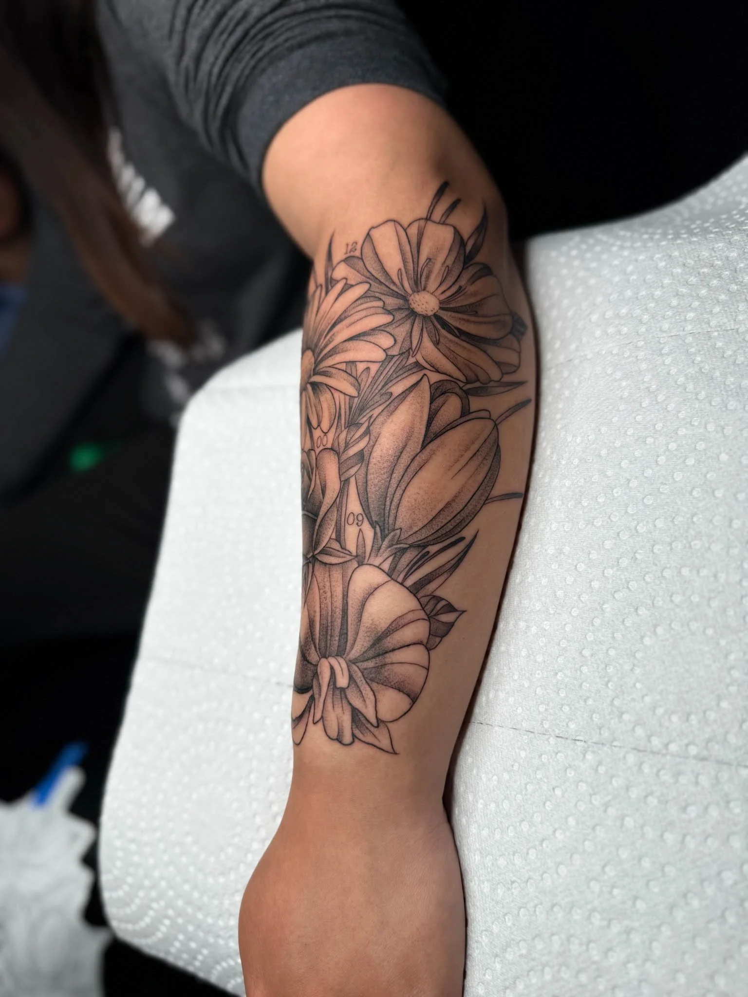 Black and gray floral tattoo on person's forearm, featuring various flowers and leaves.