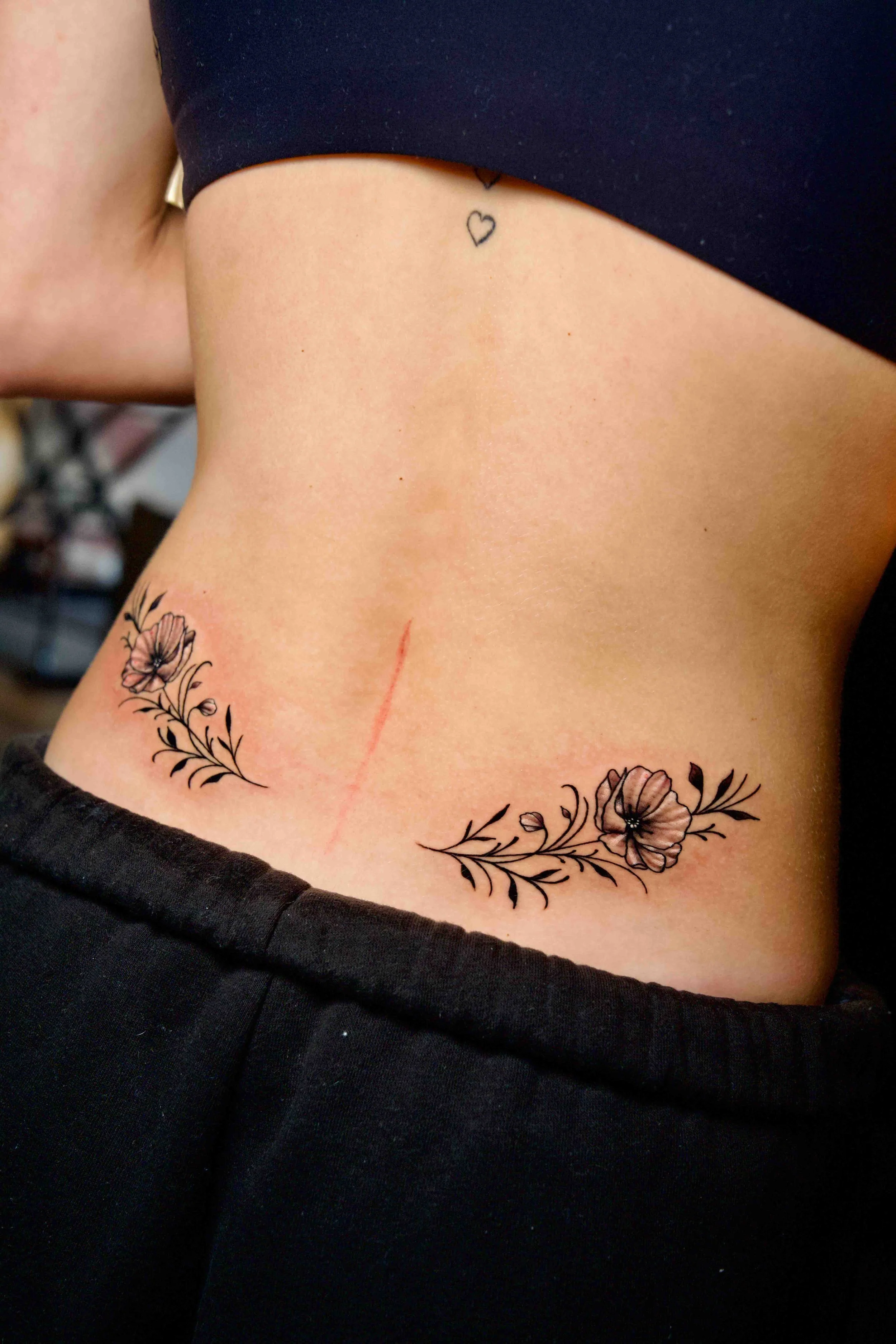 Twin floral branch tattoos stretching across a woman's lower back.