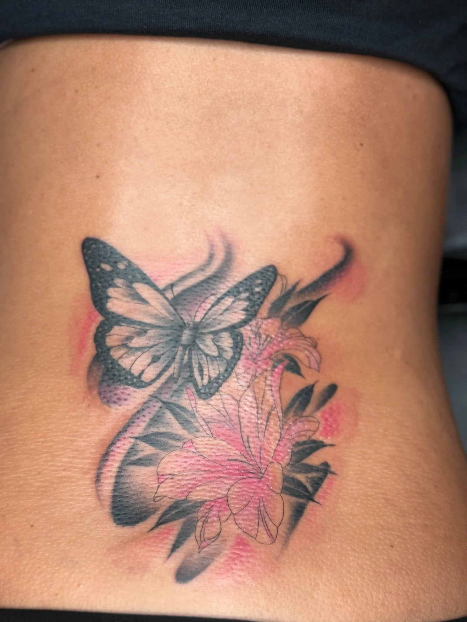 Tattoo of a butterfly with pink flowers and black leaves on skin.