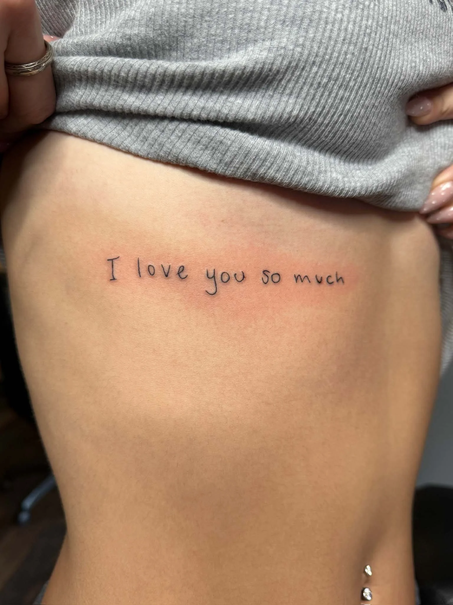 A person's side waist tattoo that says "I love you so much" in small black handwritten font.