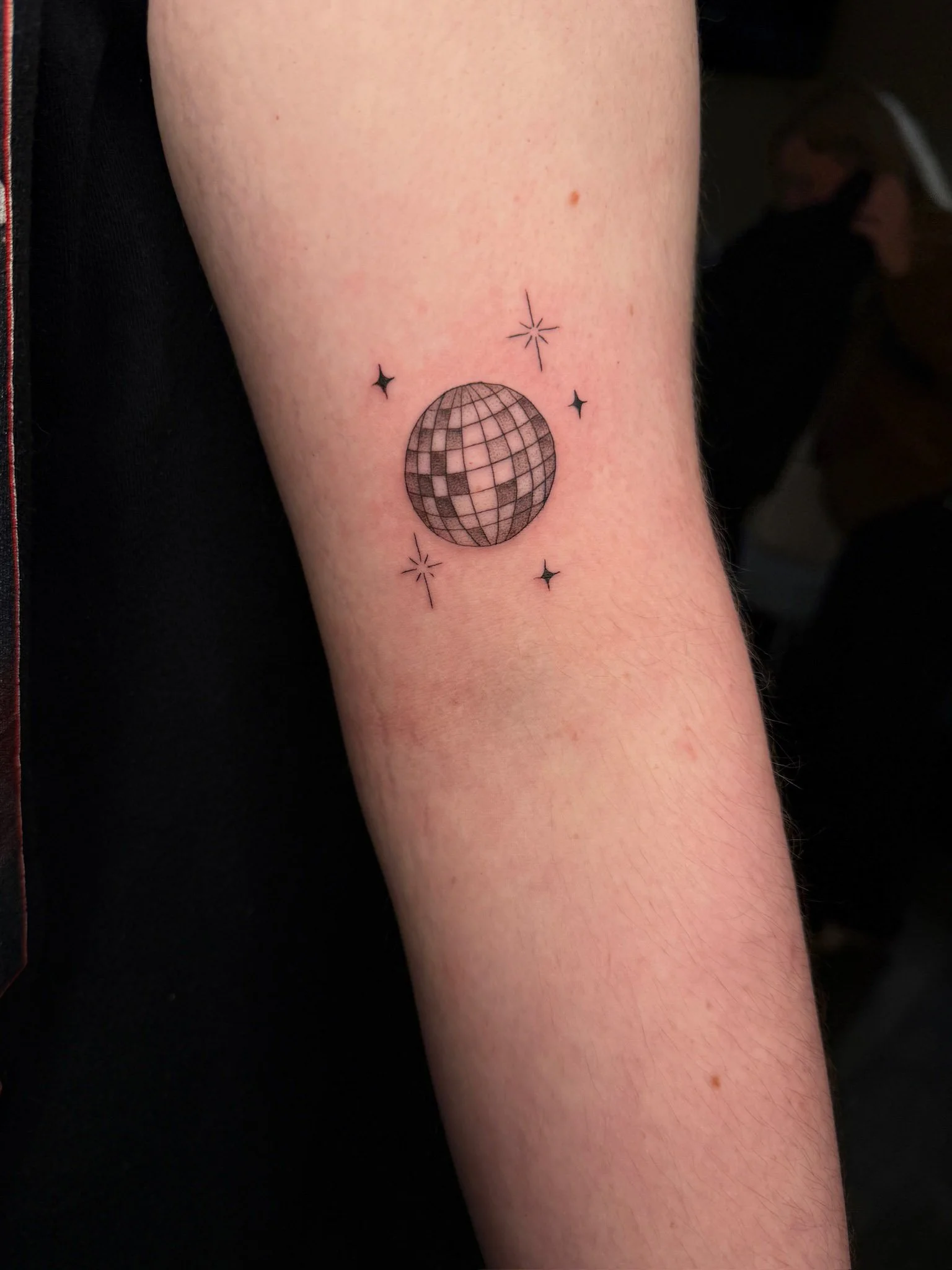 Tattoo of a disco ball surrounded by small stars on a person's arm.