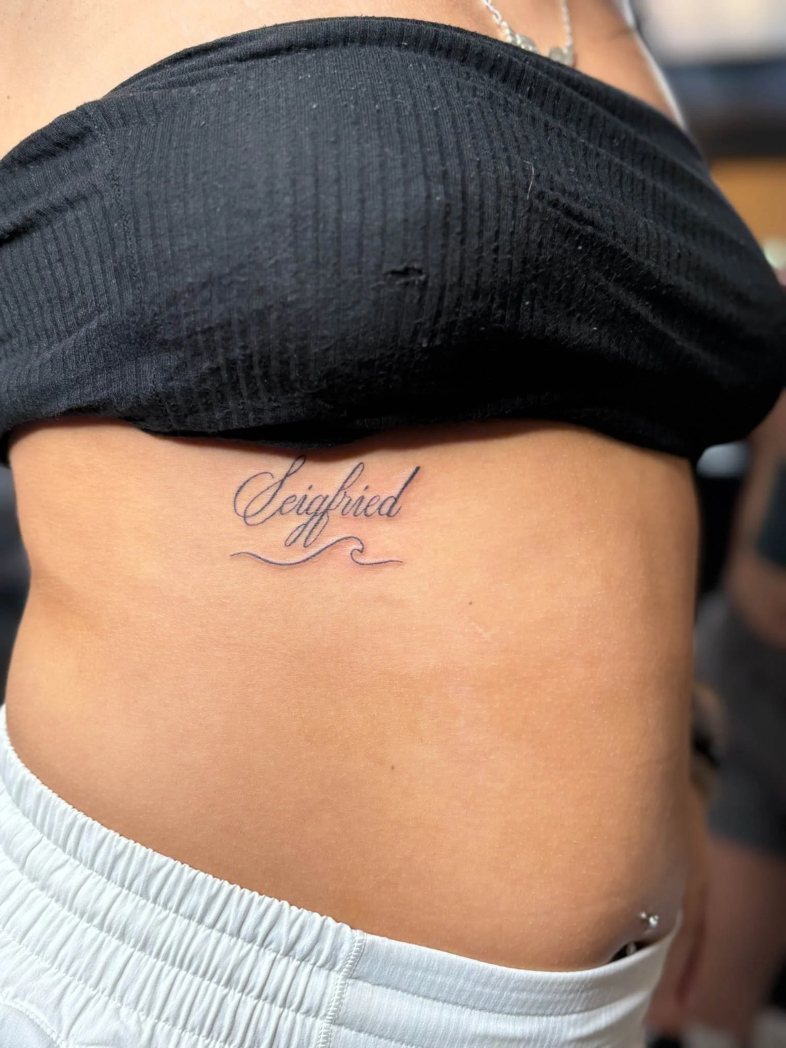 Tattoo of the word 'Siegfried' written in elegant cursive on a person's lower right abdomen.