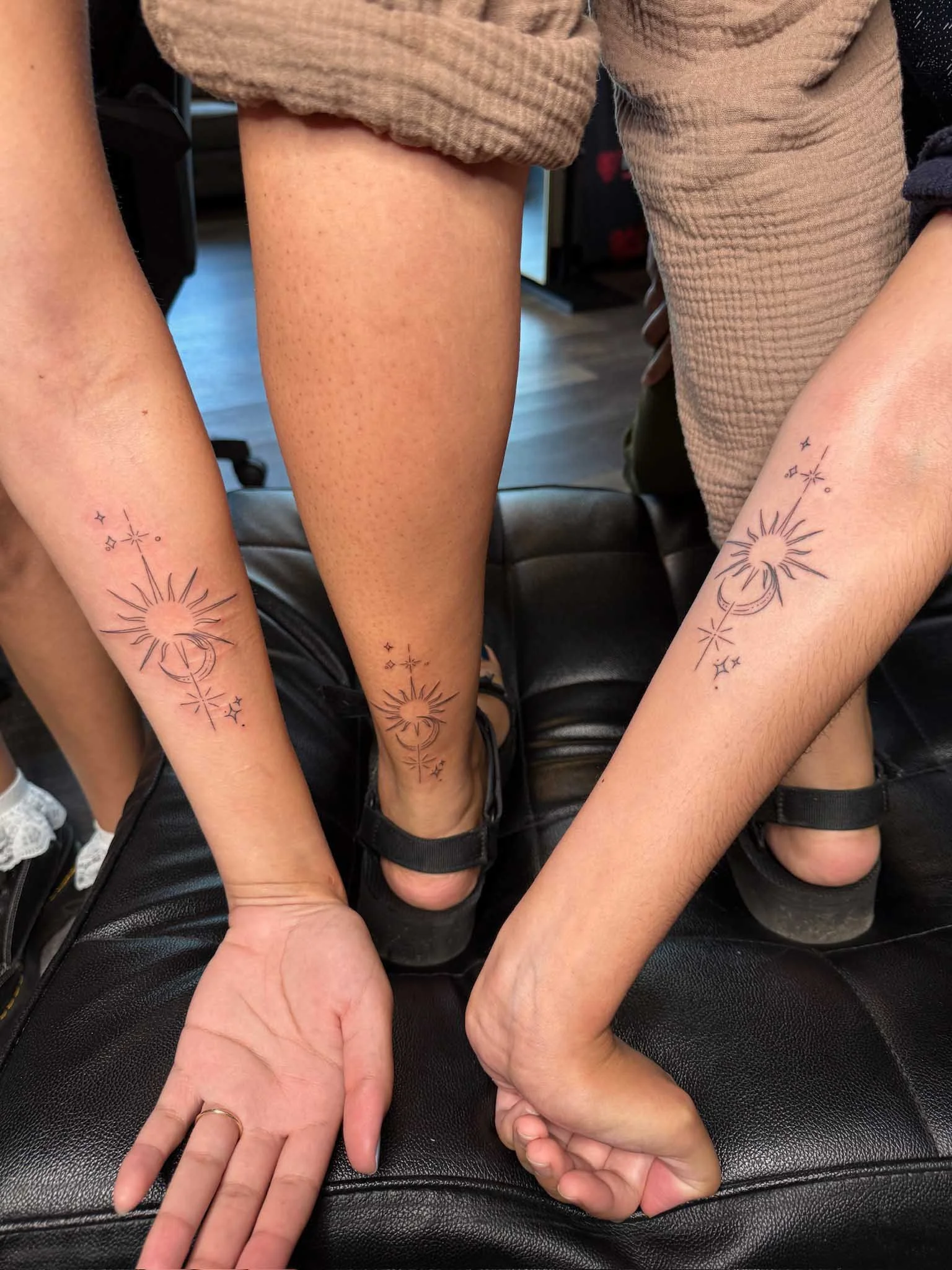 Three people with matching tattoo designs on their forearms and one person with a tattoo on their ankle, all with celestial and star motifs.