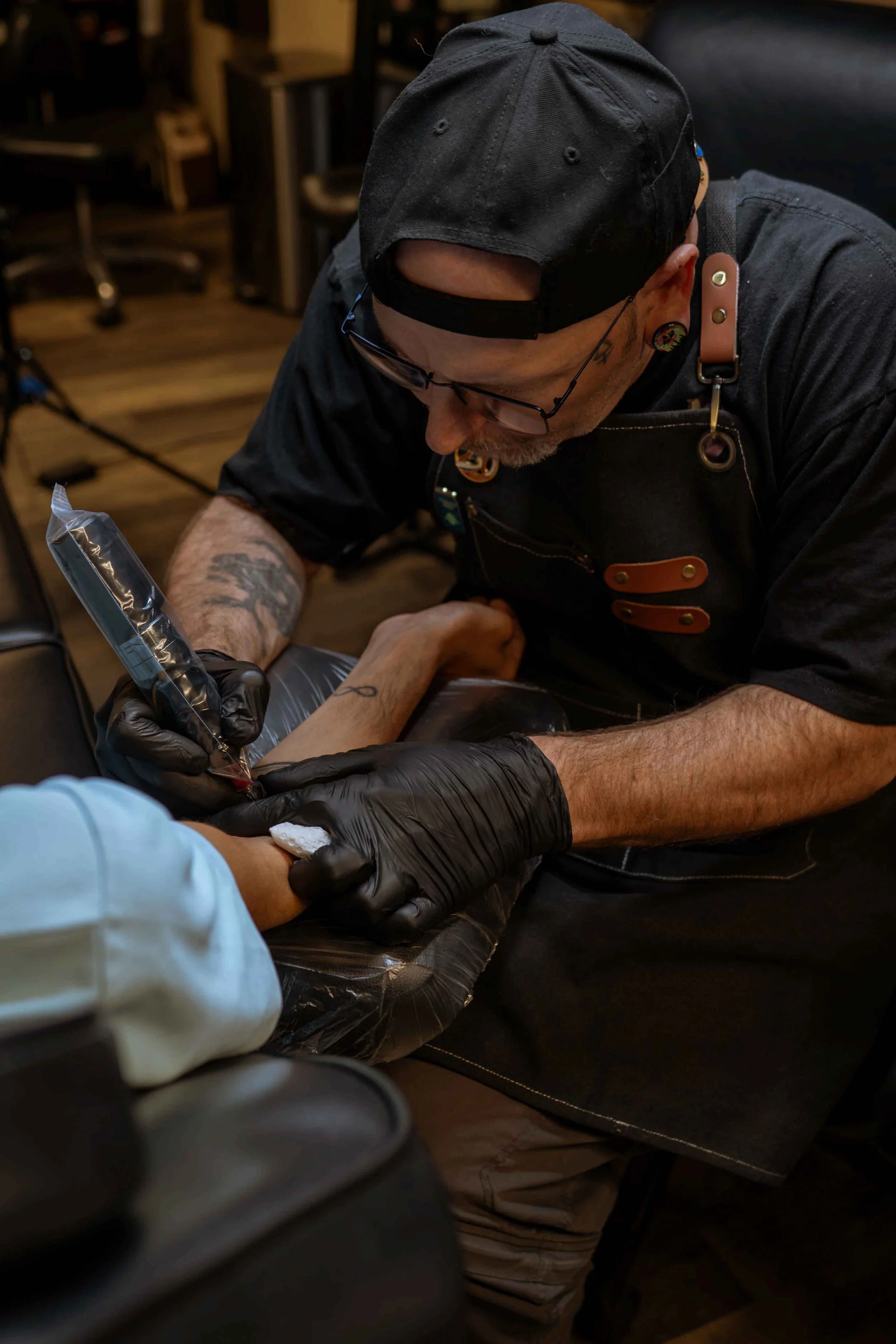 Tattoo artist in black gloves tattooing a client's upper arm.