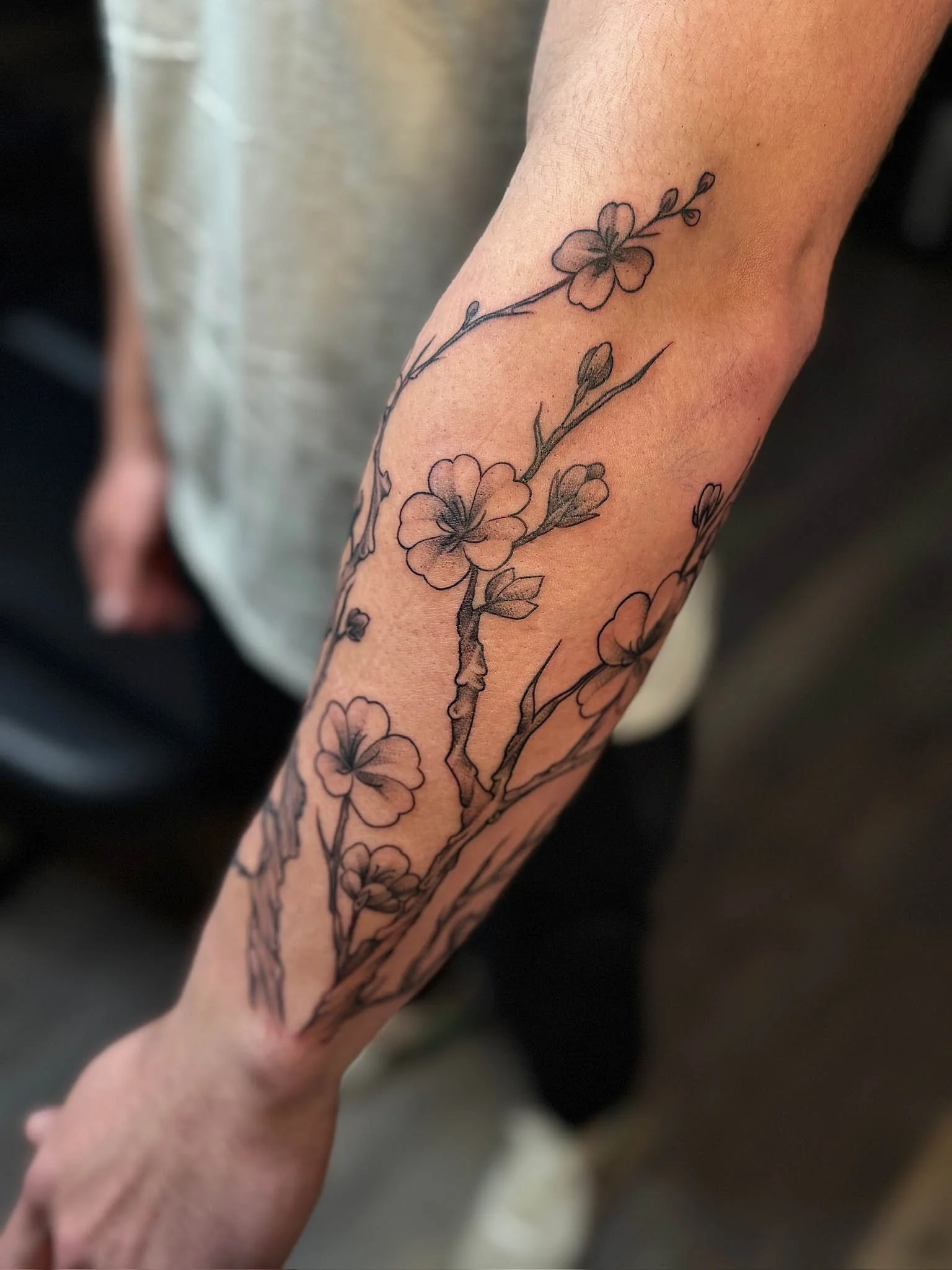 Tattoo of a flowering branch with blossoms and leaves on a person's forearm.