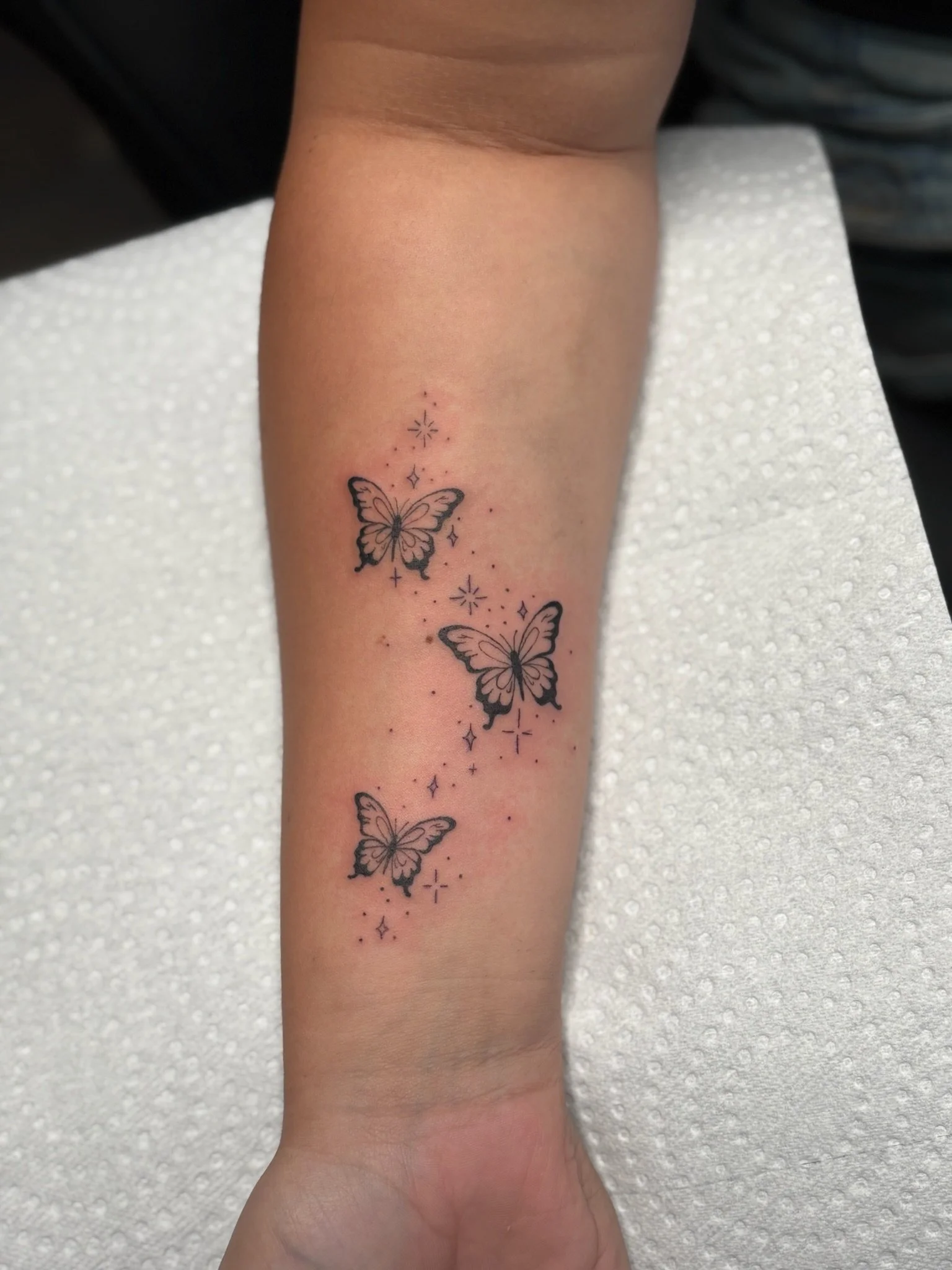 Tattoo of three butterflies with star and sparkle designs on arm