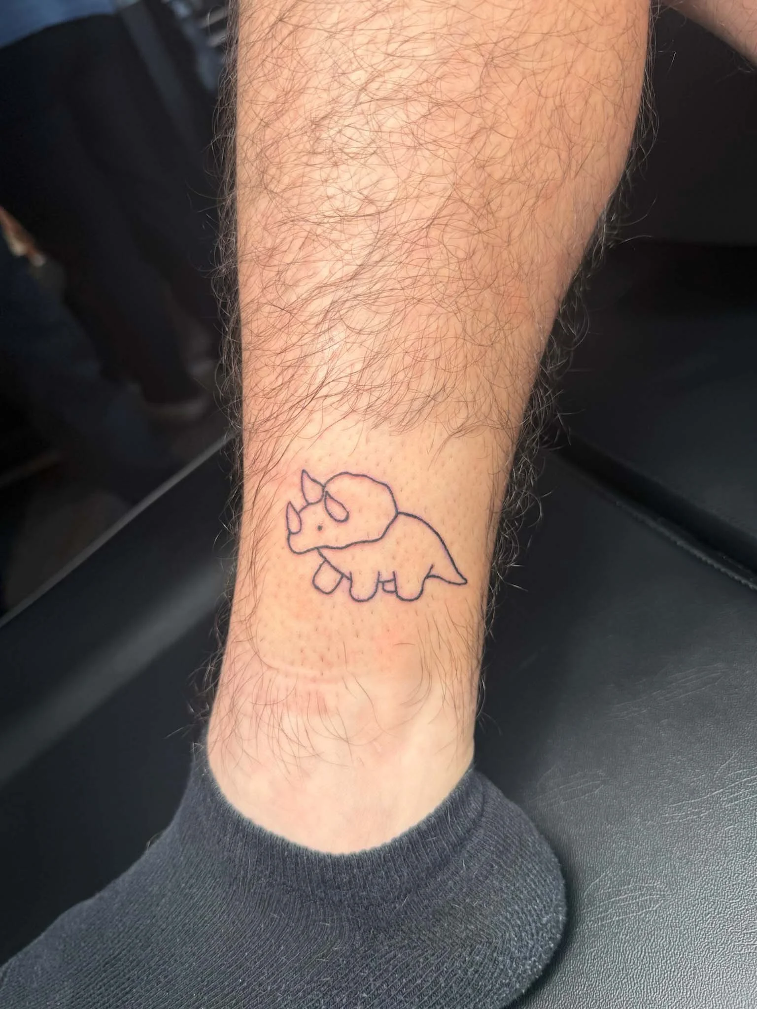 A tattoo of a cute cartoon rhinoceros with small horns and simple lines on a person's lower calf.