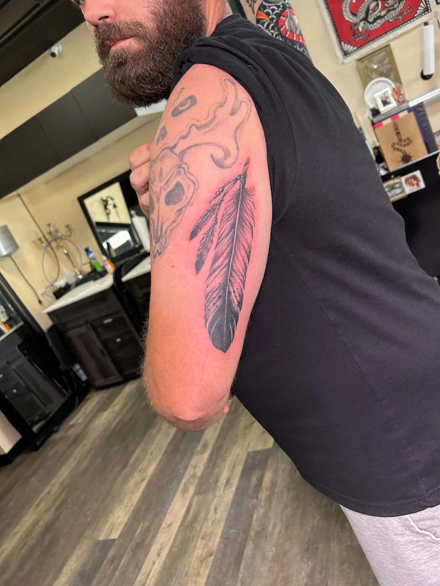 Black and grey feather tattoo on person's upper arm