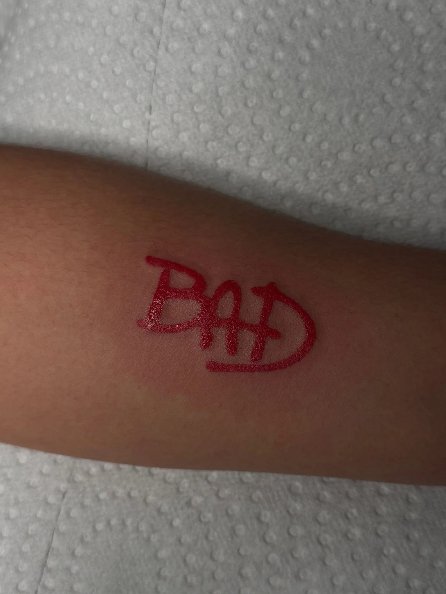 A person's arm with a red tattoo that says 'BAD' inside a speech bubble.
