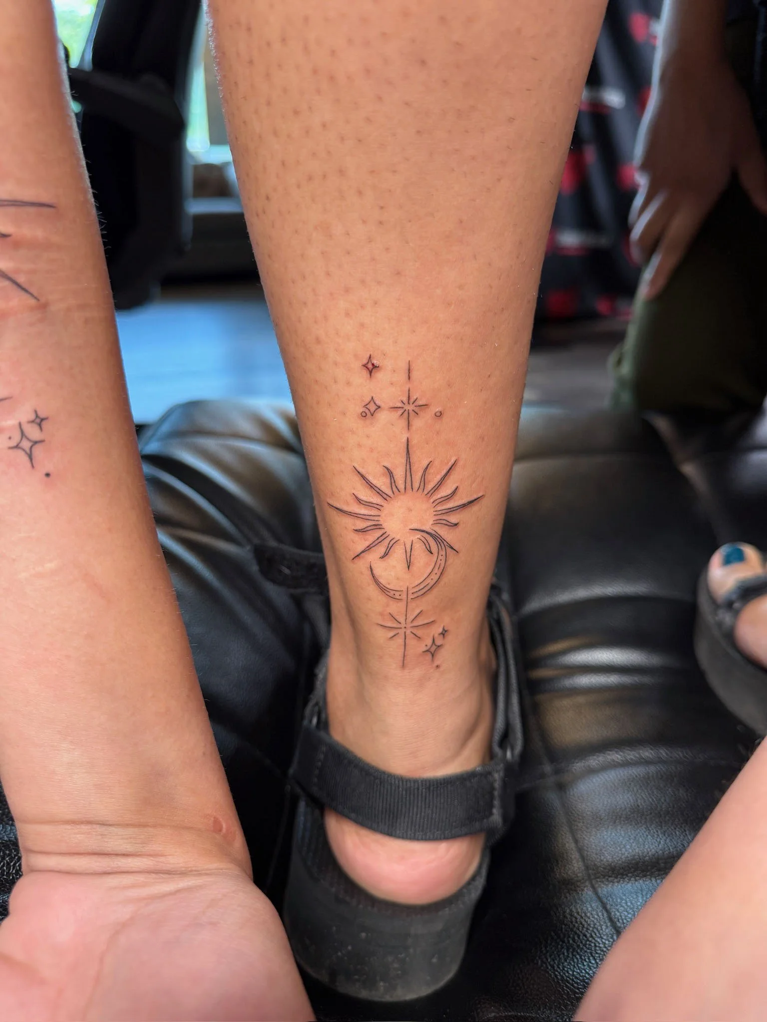 Tattoo of a crescent moon and sun with stars on the lower leg.