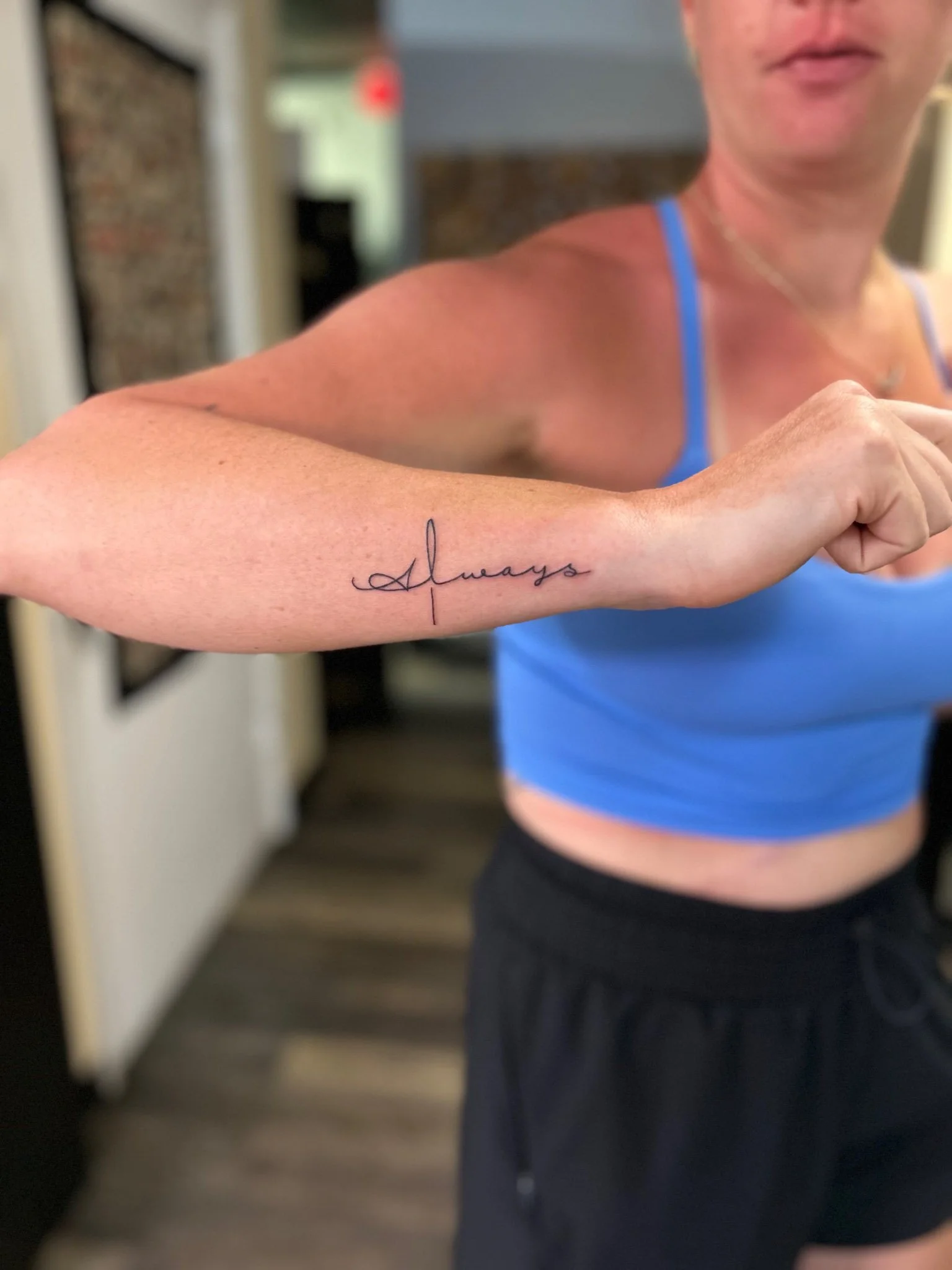 Woman in a blue tank top extending her arm to show a fine-line forearm tattoo
