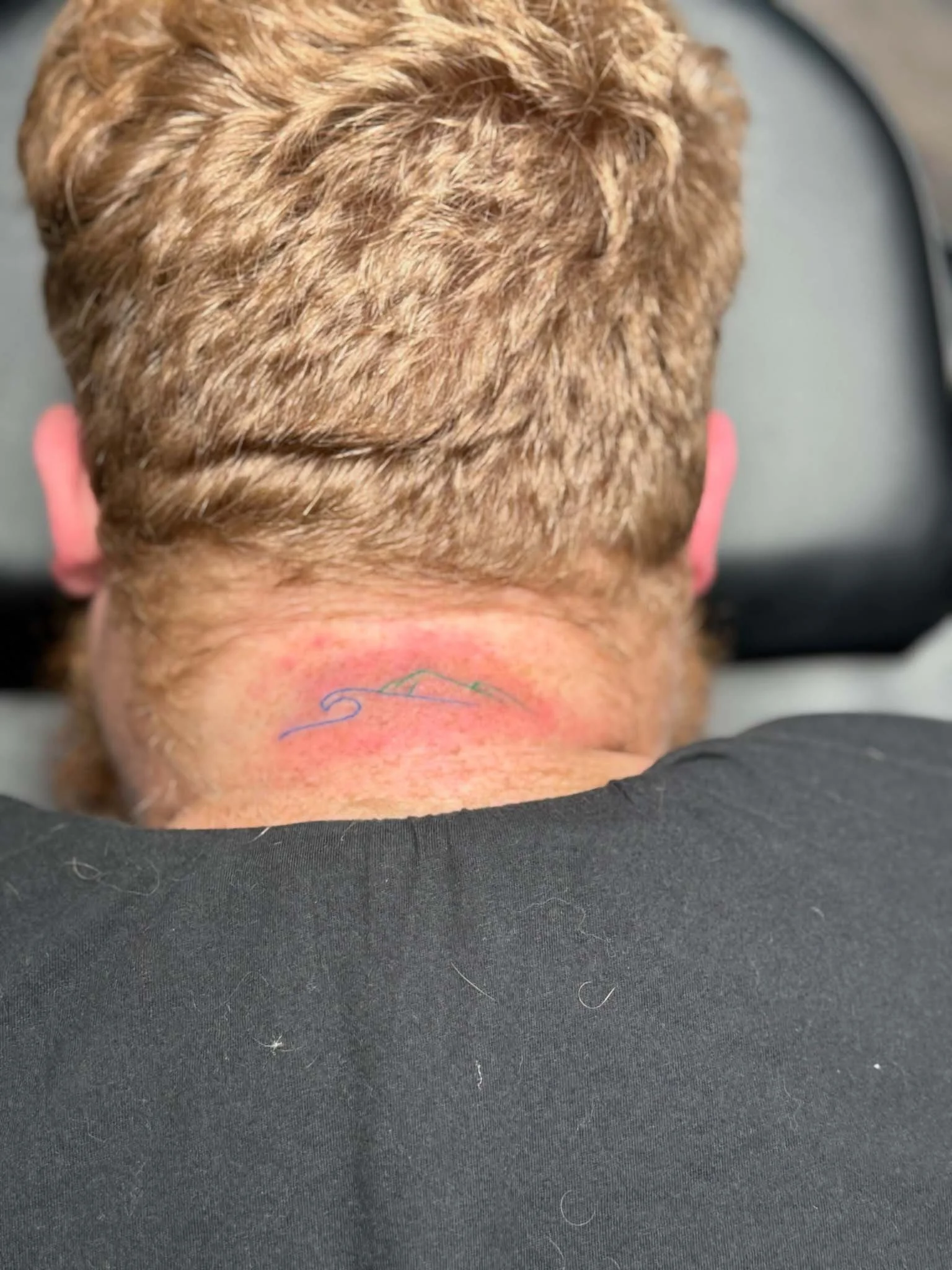 Back of a person's head with newly shaved hair and a small line drawing on the neck, sitting in a chair.