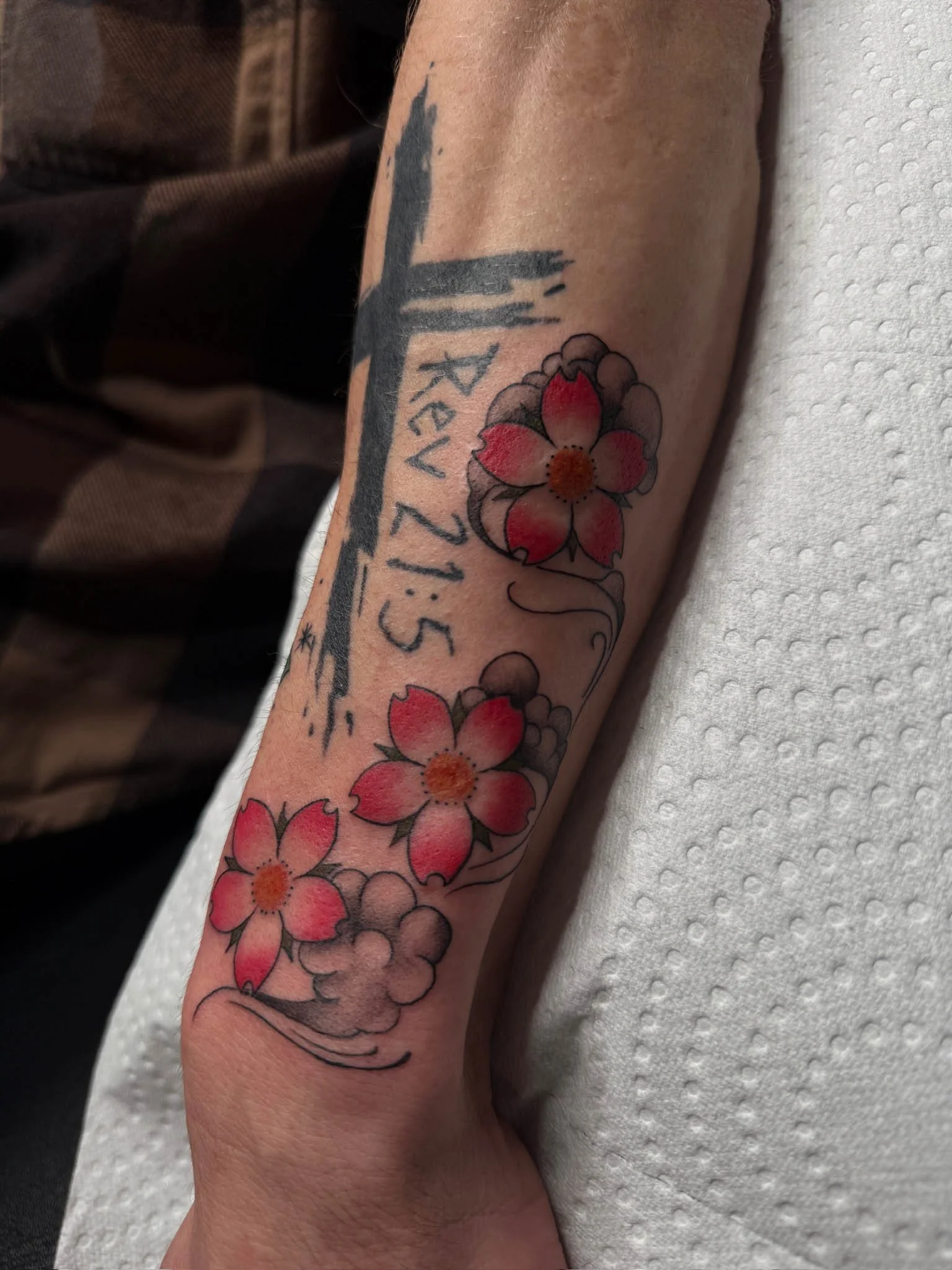 Tattoo of pink and red cherry blossoms with gray cloud and black ink accents on person's forearm.